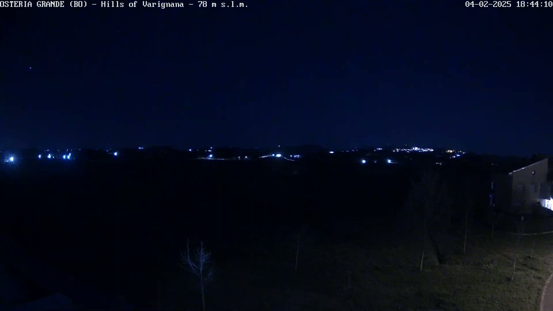 A nighttime view of dimly lit hills and a few buildings under a clear, dark sky.