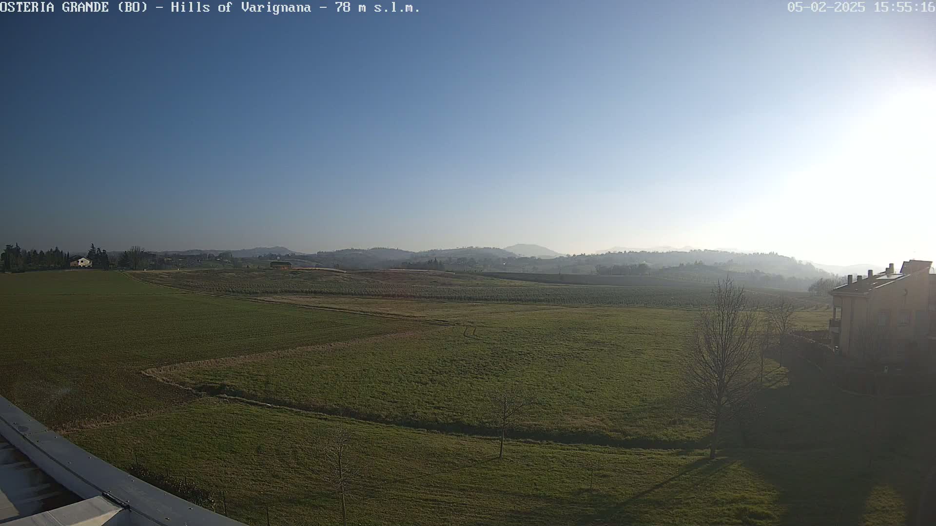 A clear, sunny day reveals a wide expanse of green fields and distant hills, with a few buildings visible in the foreground and background.