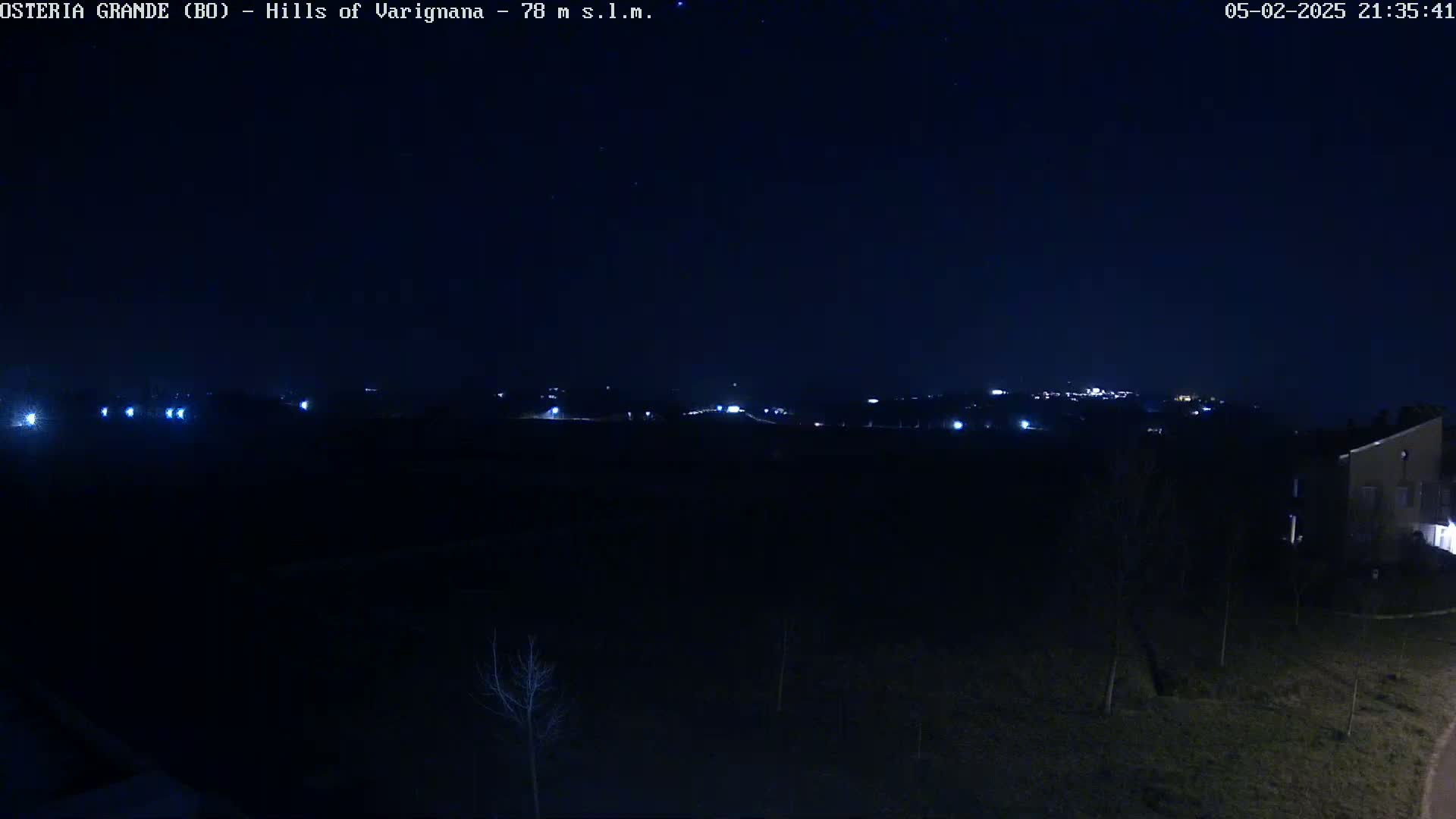 A nighttime, outdoor view shows a dark landscape with a few distant lights and a building on the right side.