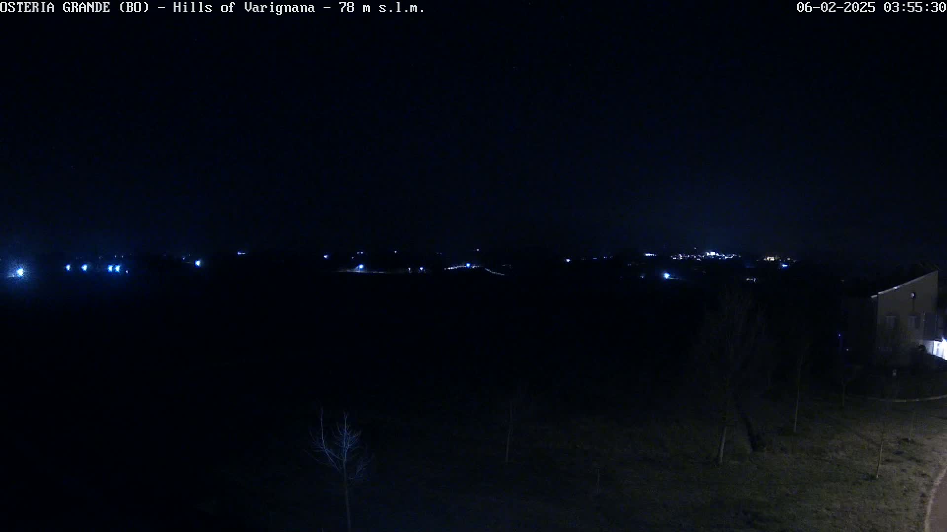 A nighttime view of dimly lit hills and a few buildings under a clear, dark sky.