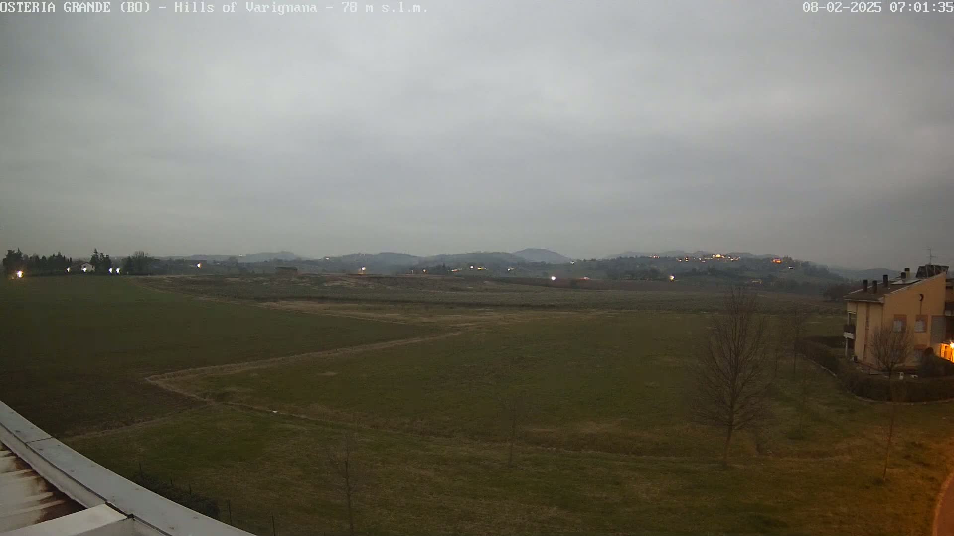 A flat, grassy field stretches to distant, dimly lit hills under a cloudy, overcast sky.