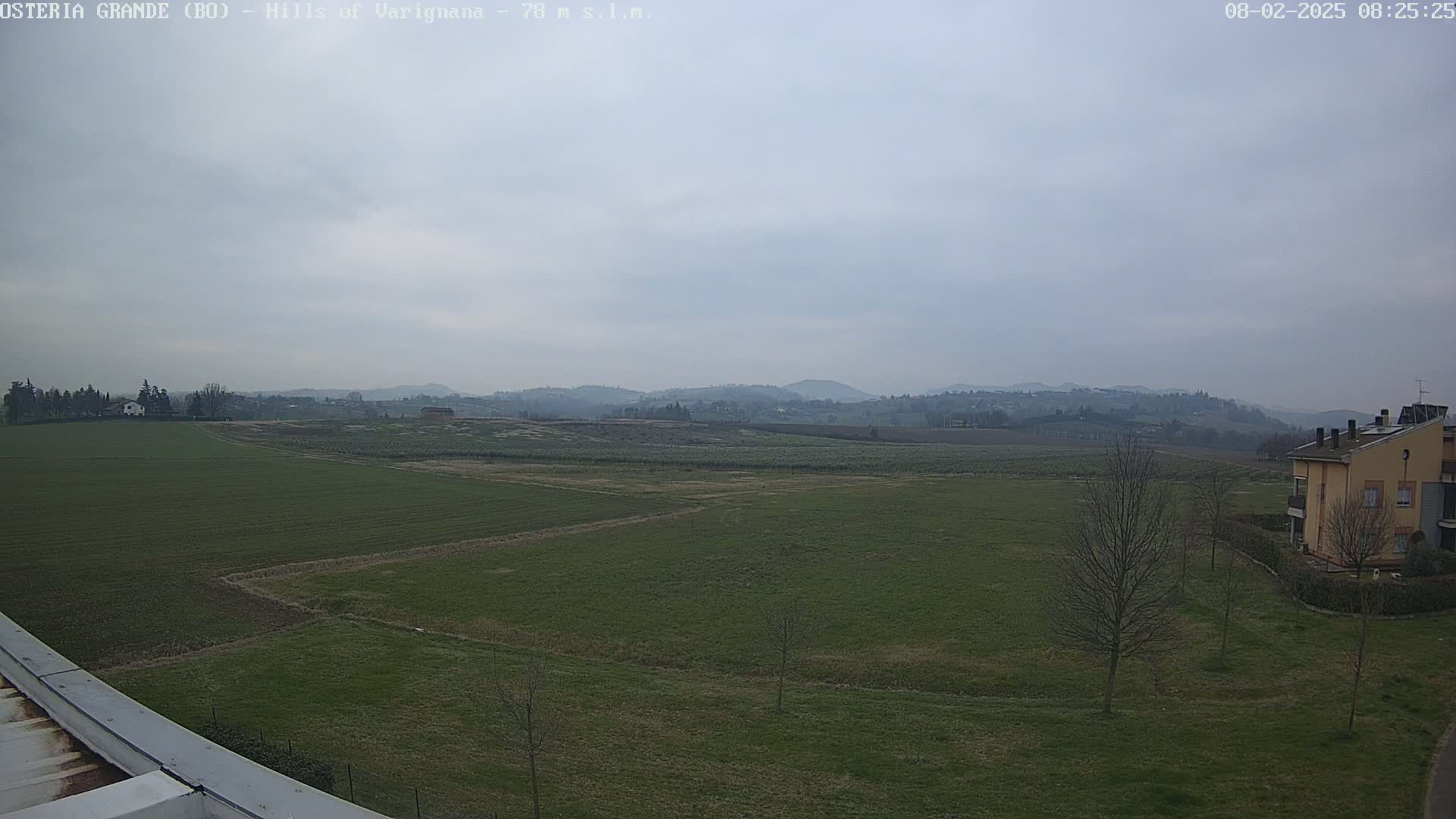 A wide, flat expanse of green farmland stretches to rolling hills under a cloudy sky.