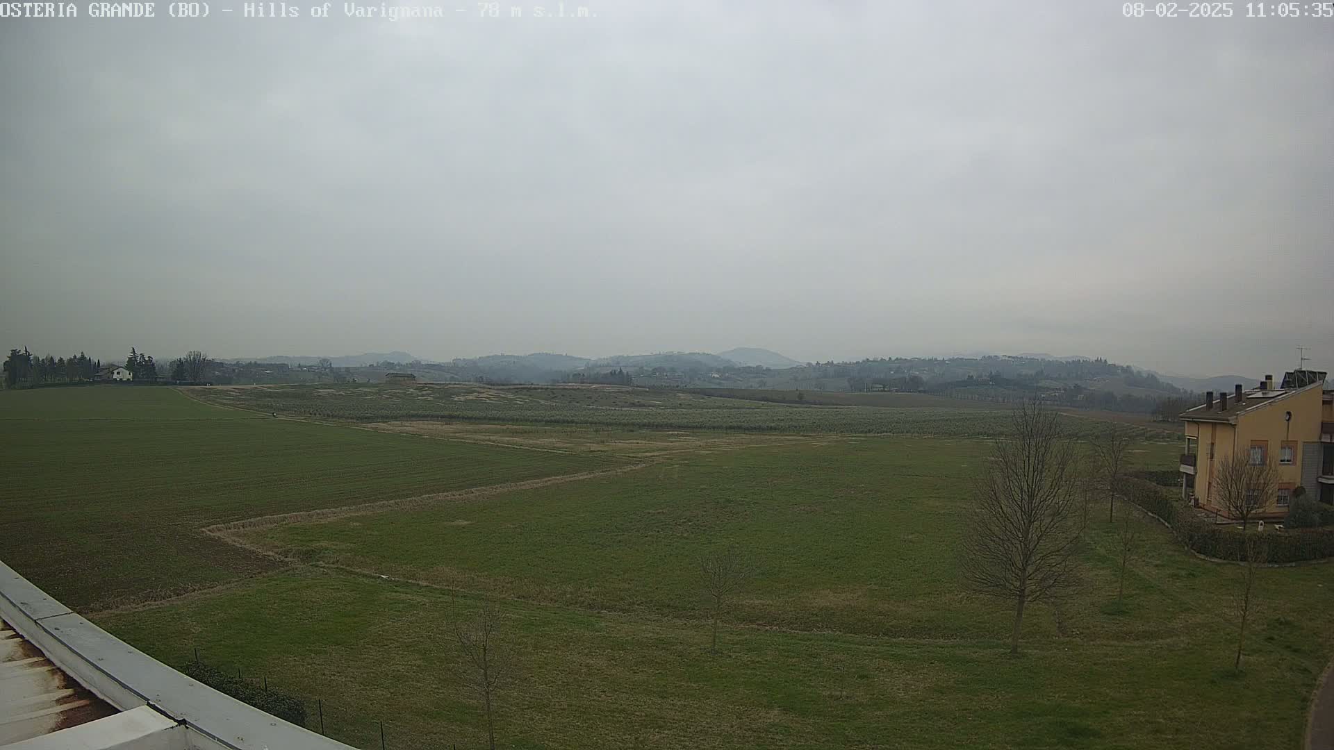 A flat expanse of green farmland stretches to rolling hills under an overcast sky.