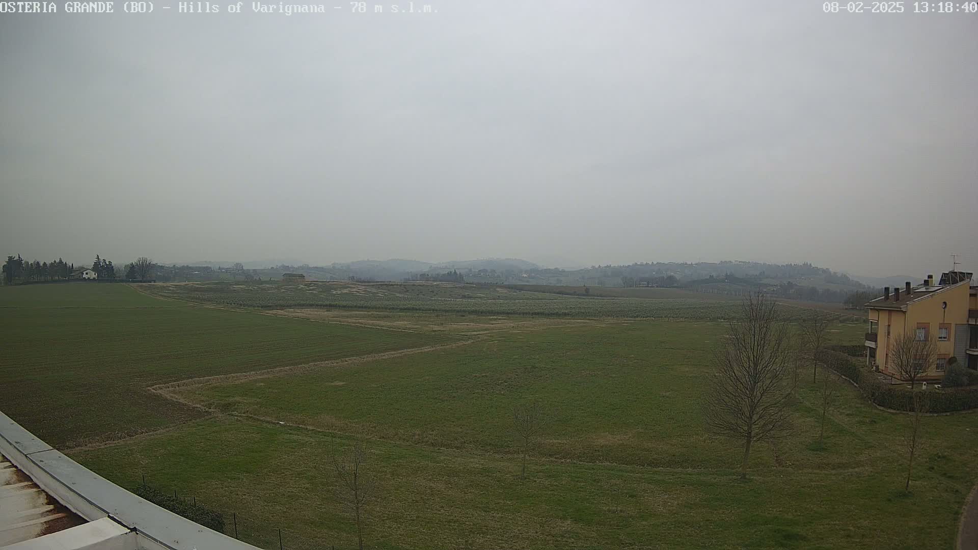 A hazy view of flat, green farmland stretches to rolling hills under a gray sky.
