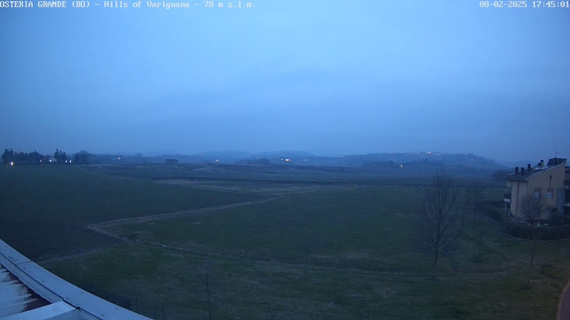 A twilight view shows flat, dark green fields extending to distant hills under a hazy, blue-gray sky.
