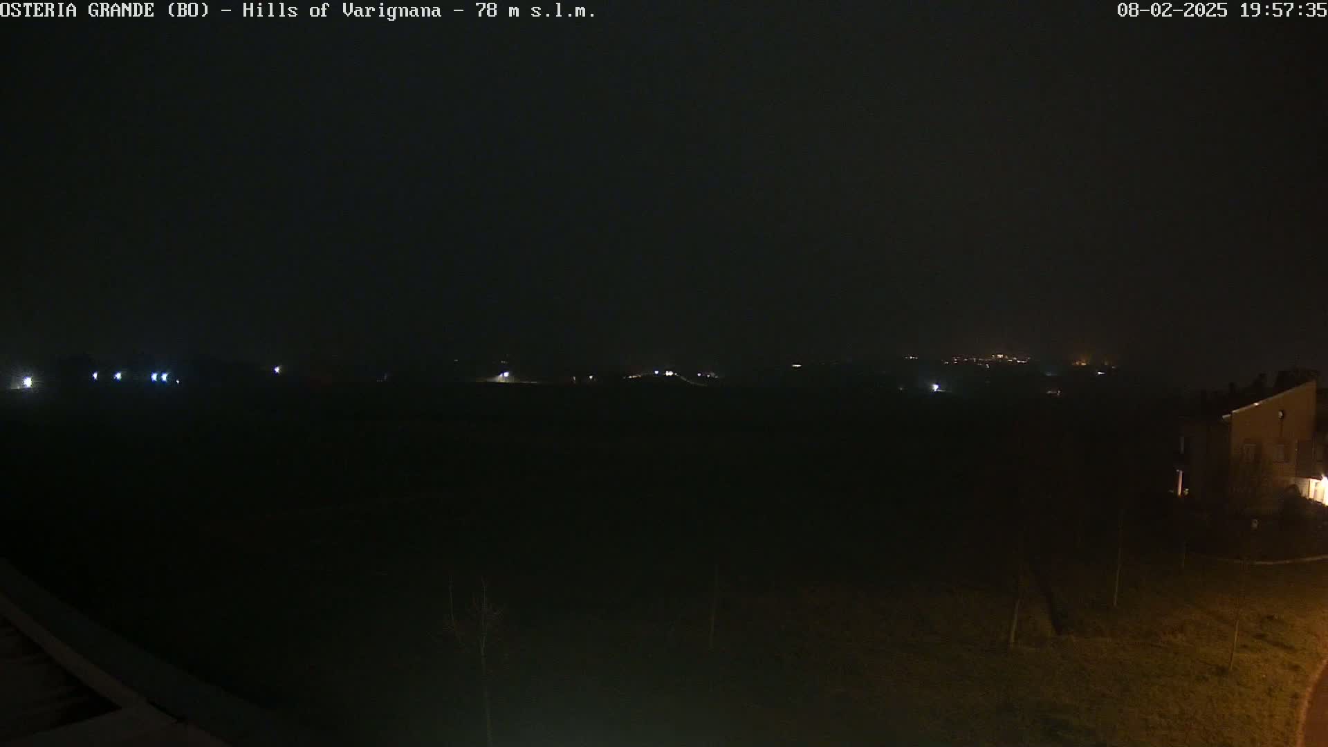 A dark, nighttime landscape is visible, showing a few distant lights and a building in the lower right corner under a clear, dark sky.