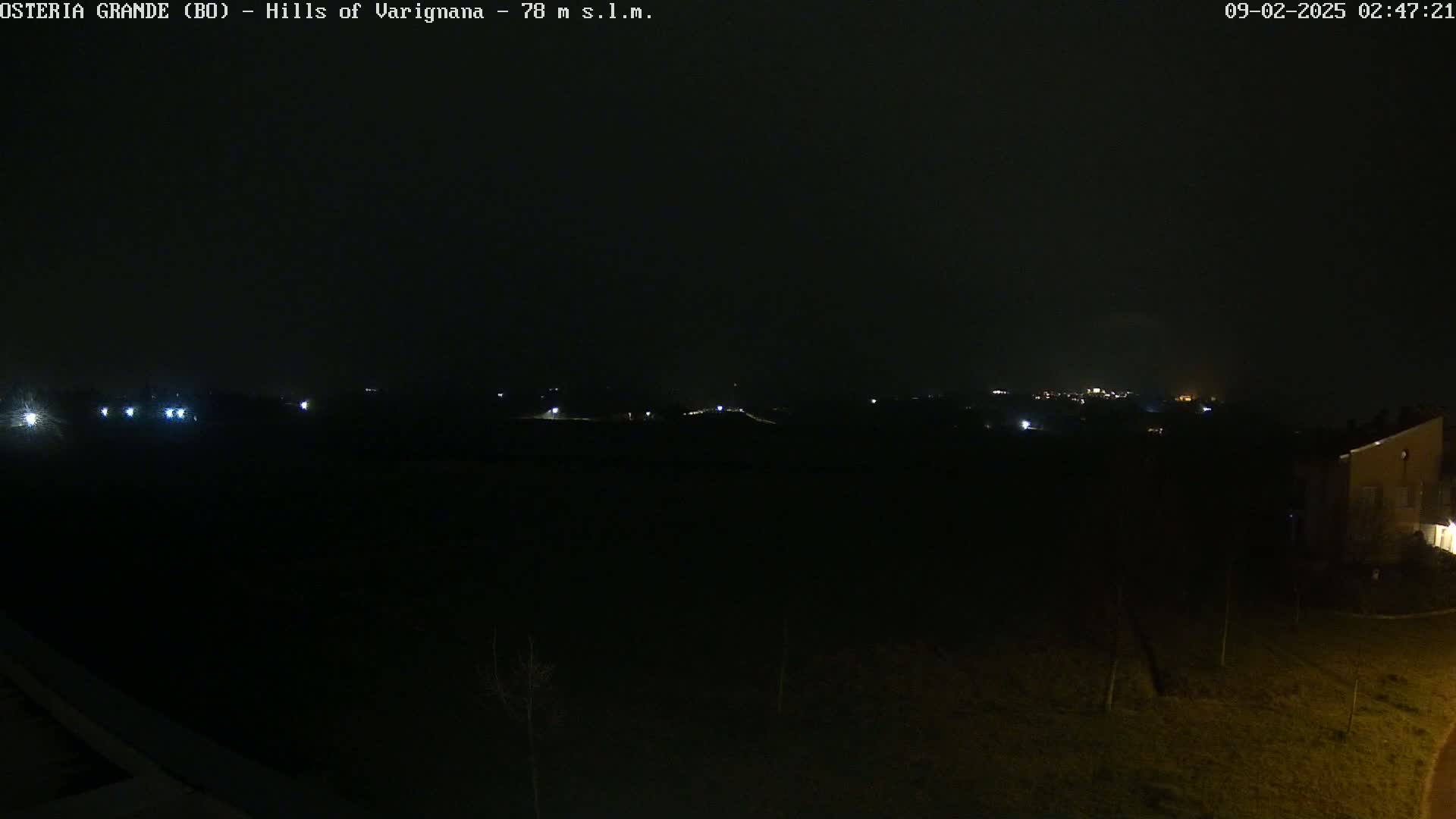 A dark, nighttime landscape with a few distant lights visible under an overcast sky.