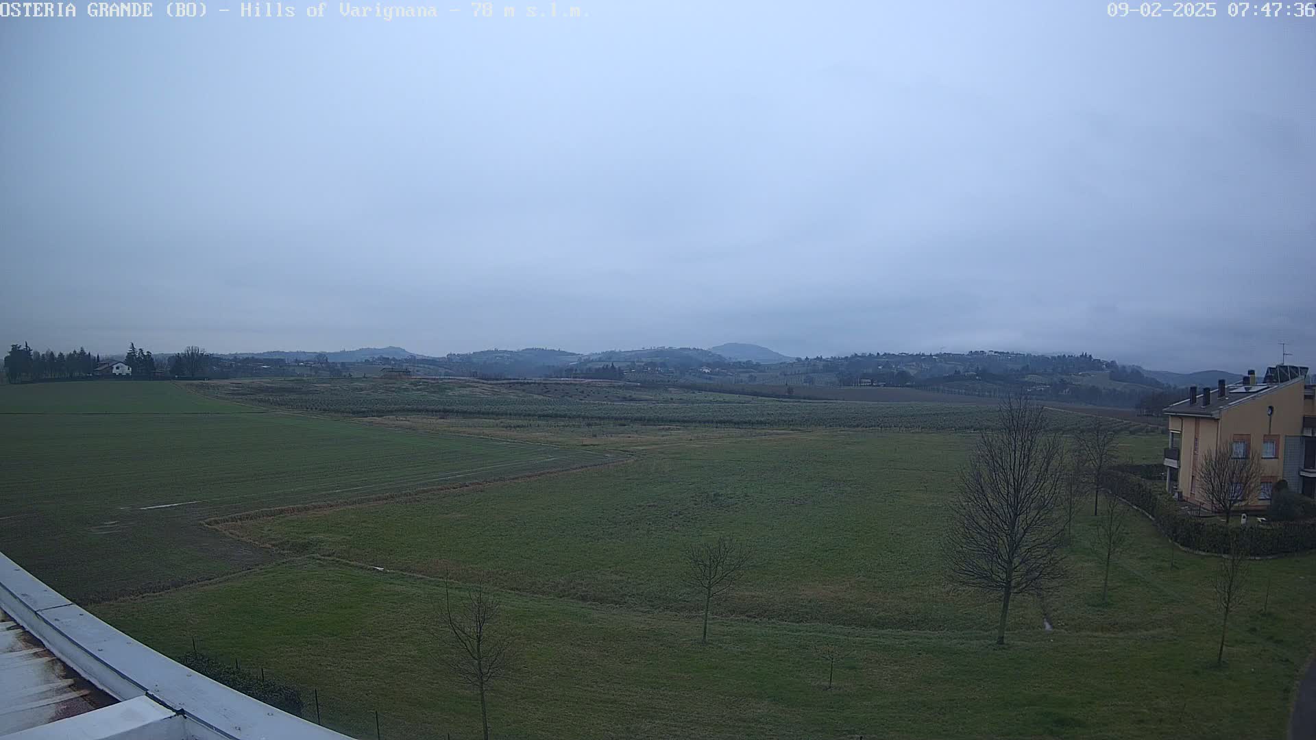 A wide, flat expanse of green farmland stretches to a line of low hills under an overcast sky.