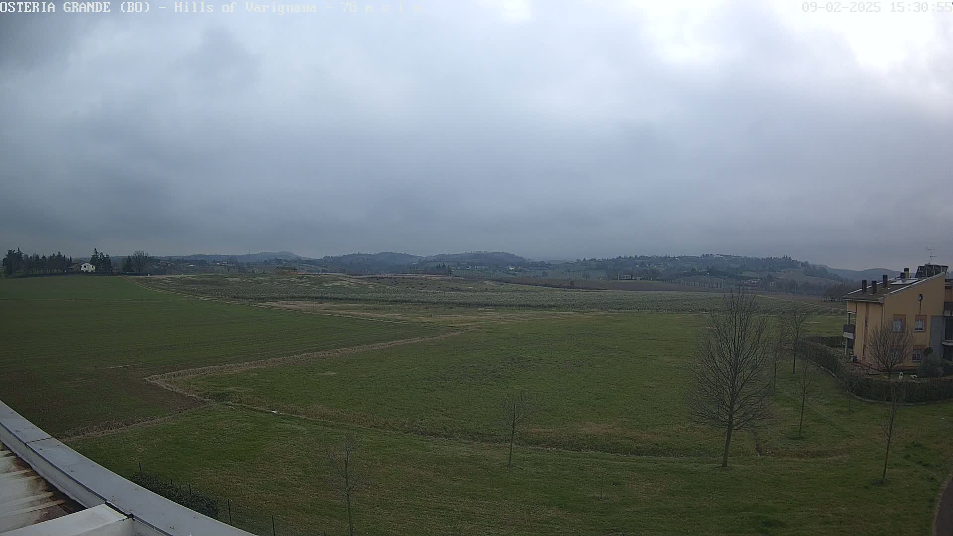 A wide, flat expanse of green farmland stretches to rolling hills under a cloudy sky.
