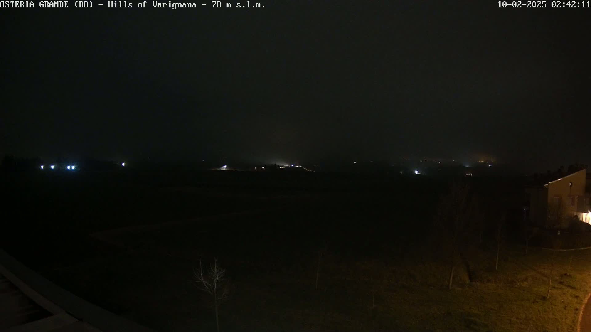 A dark, foggy nighttime landscape shows dimly lit buildings and distant lights in the hazy distance.