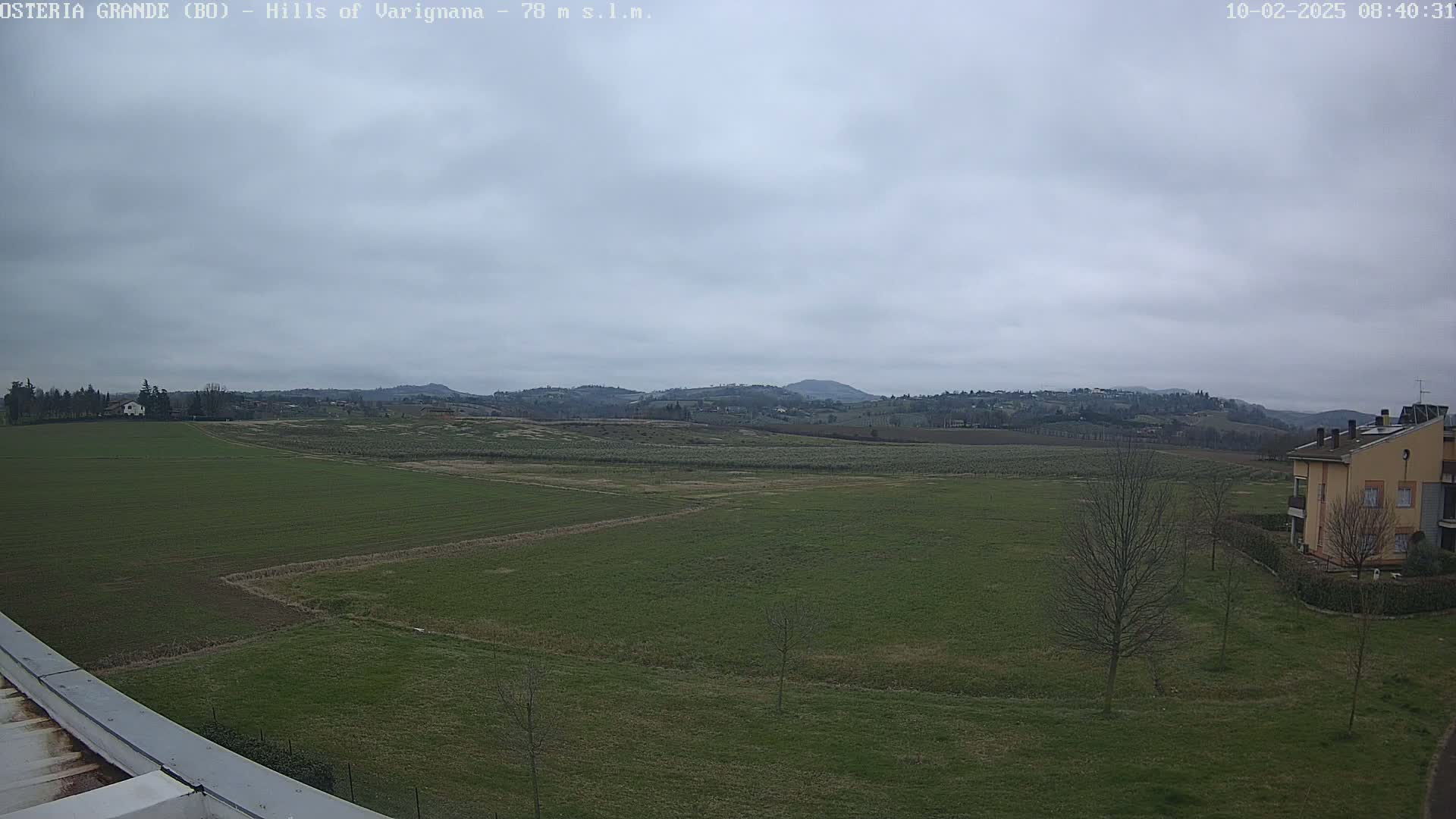A wide, flat expanse of green farmland stretches to rolling hills under an overcast sky.