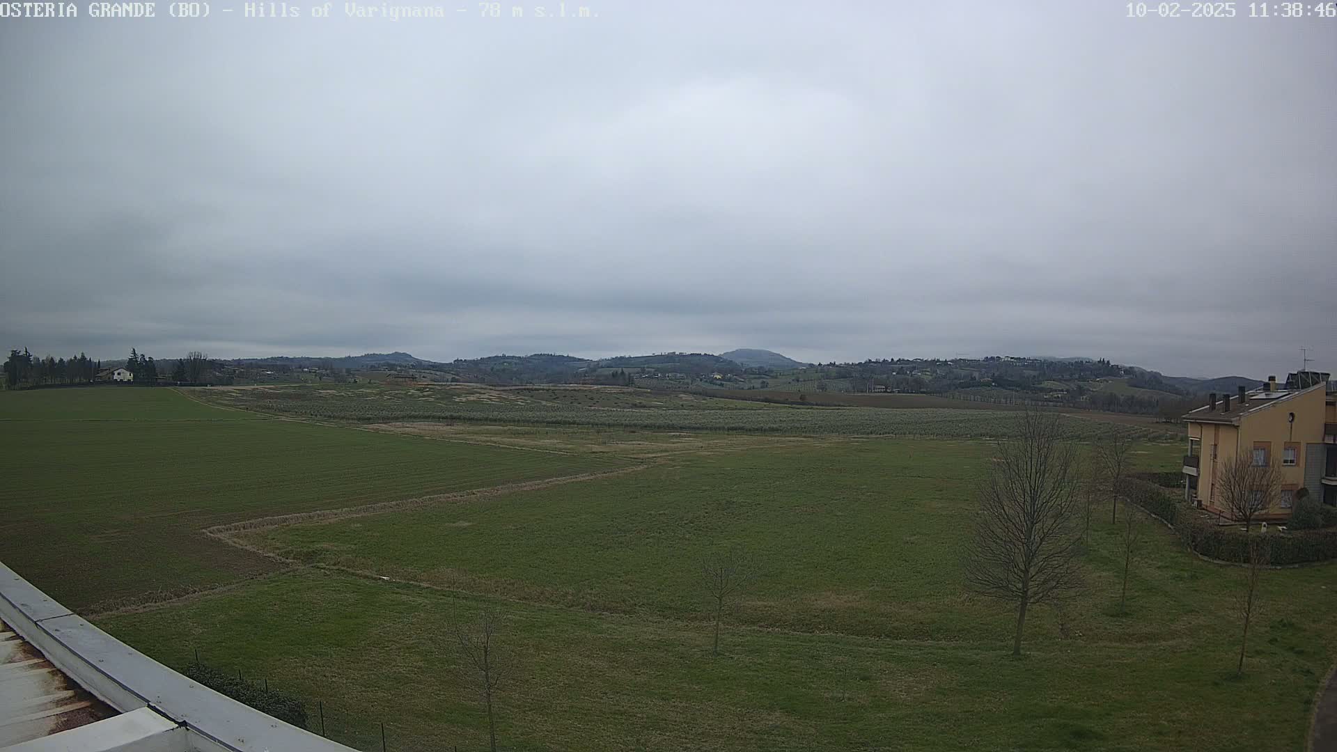 A flat, green field stretches towards rolling hills under an overcast sky.