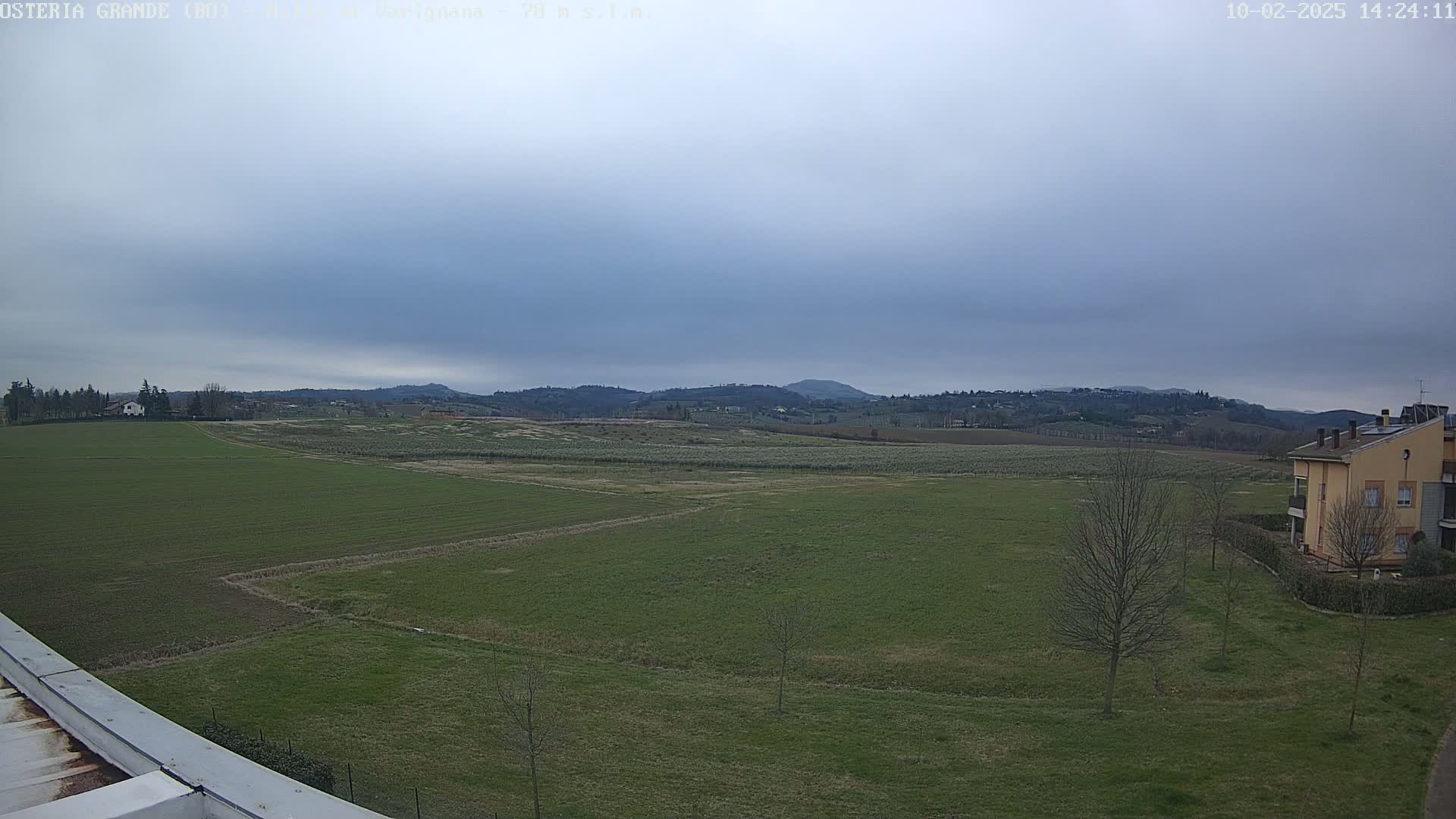 A wide, flat expanse of green fields stretches toward distant, rolling hills under a cloudy sky.
