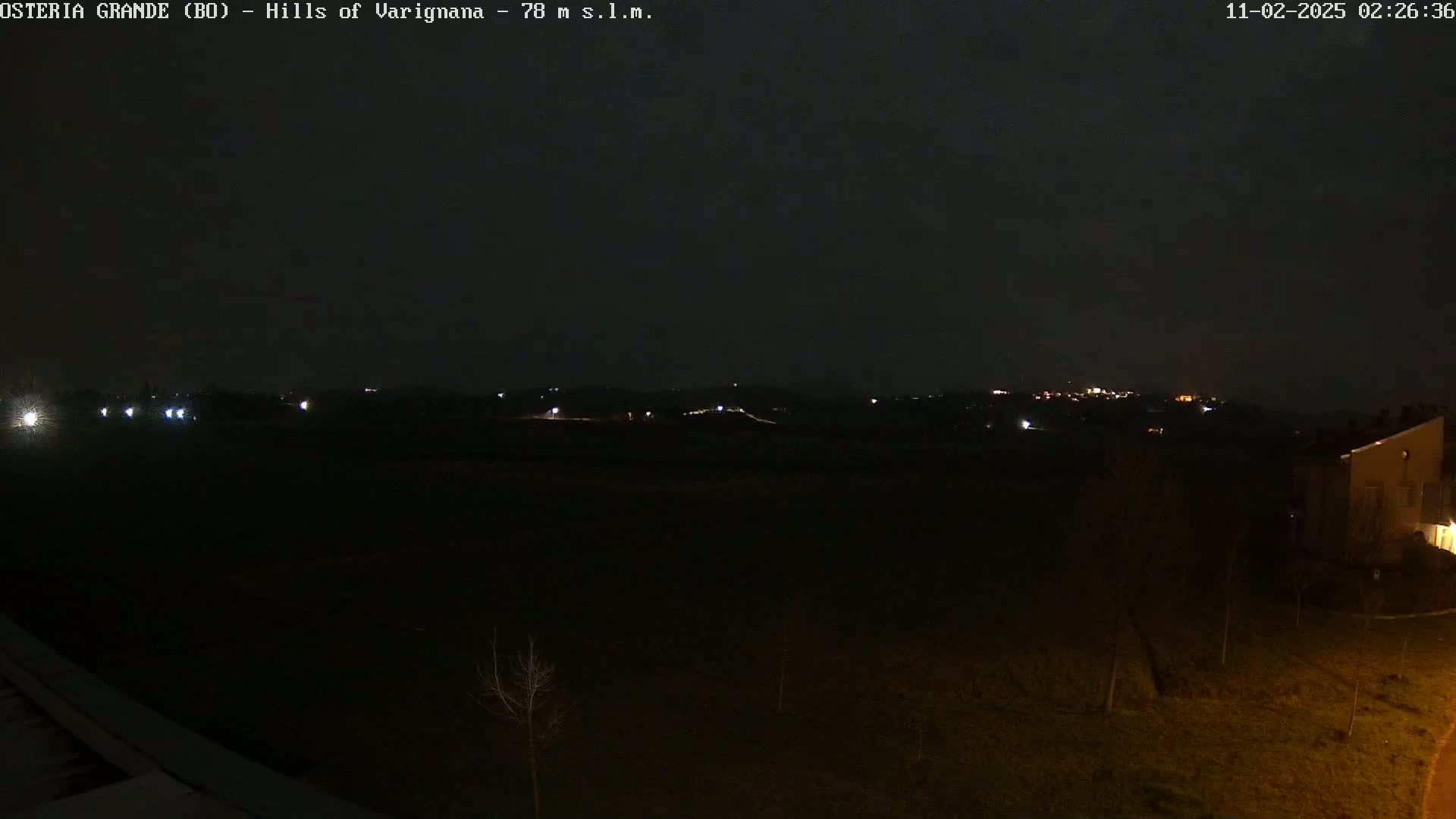 A nighttime view of dark hills and fields dotted with a few distant lights, under a clear, dark sky.