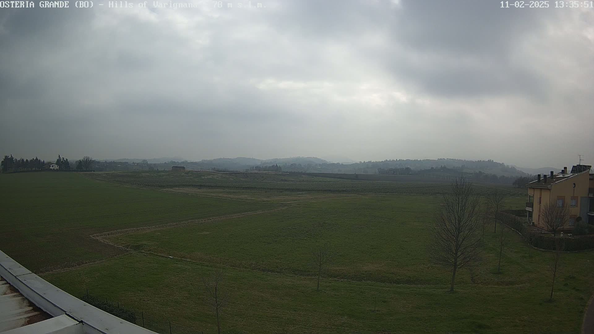 A wide, flat expanse of green fields stretches toward distant, rolling hills under a hazy, overcast sky.