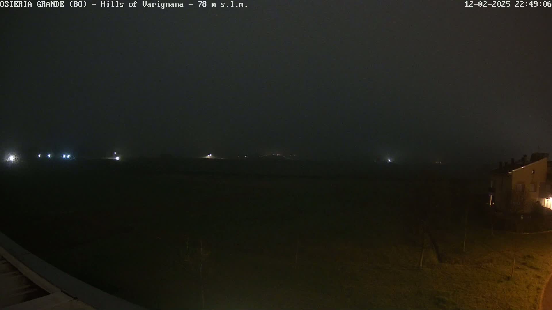 A dark, foggy nighttime scene shows a few distant lights and a building in the lower right corner.