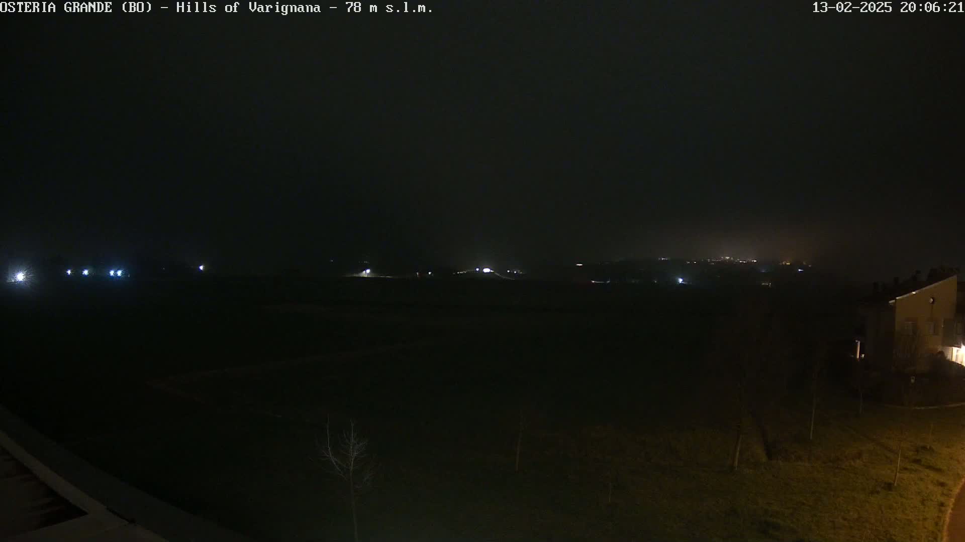 A dark, nighttime landscape is visible, with a few distant lights and a building in the lower right corner under a hazy sky.