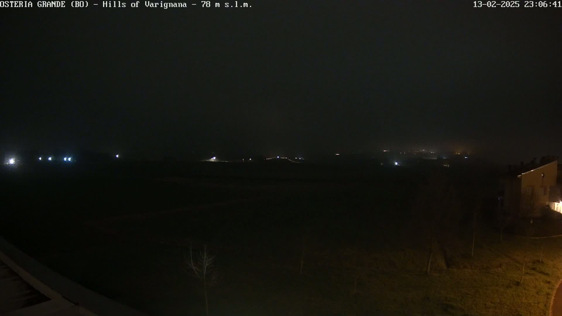 A nighttime, foggy view of dimly lit fields and buildings in the distance.