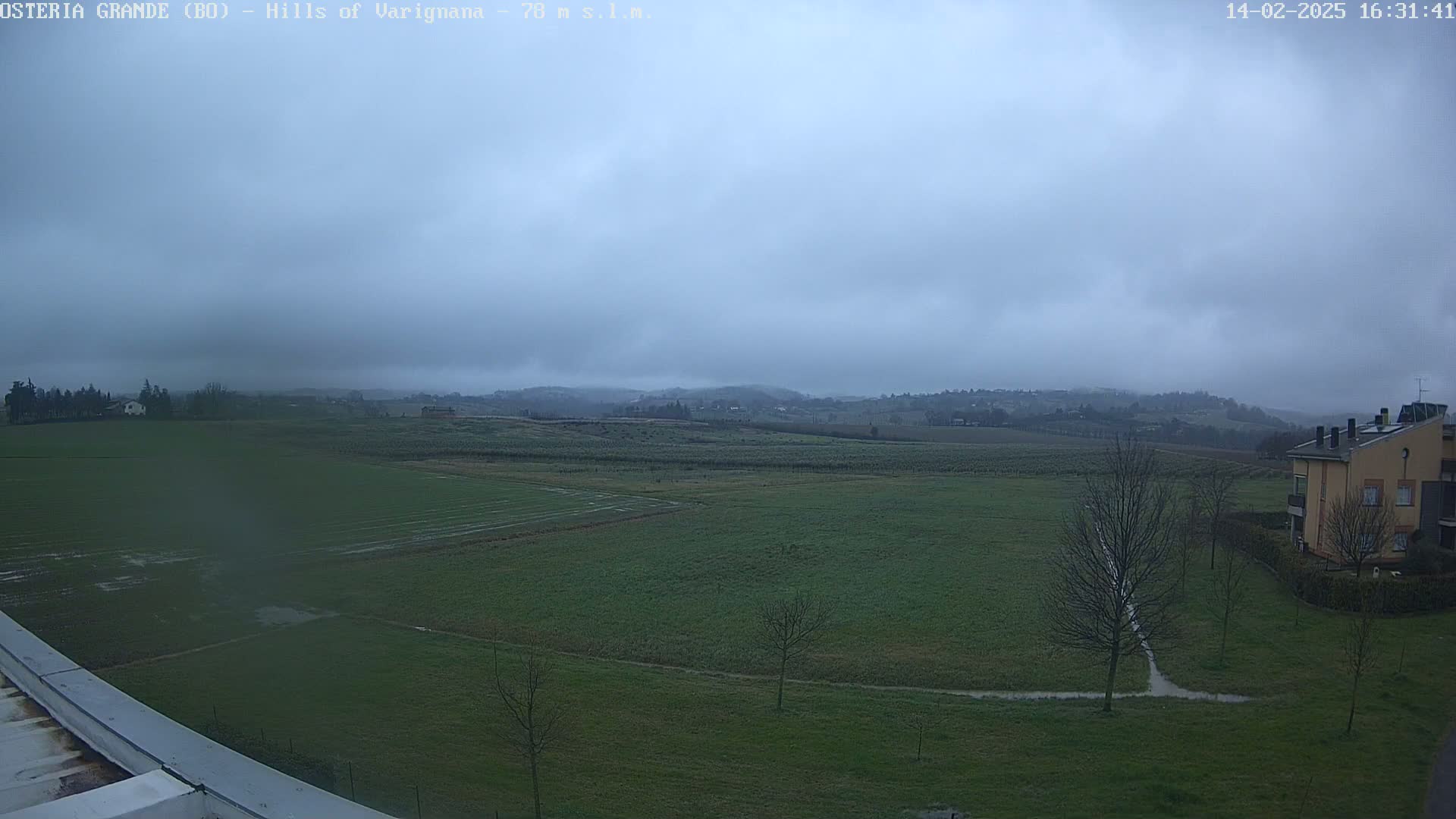 A flat, green field stretches to rolling hills under an overcast sky.
