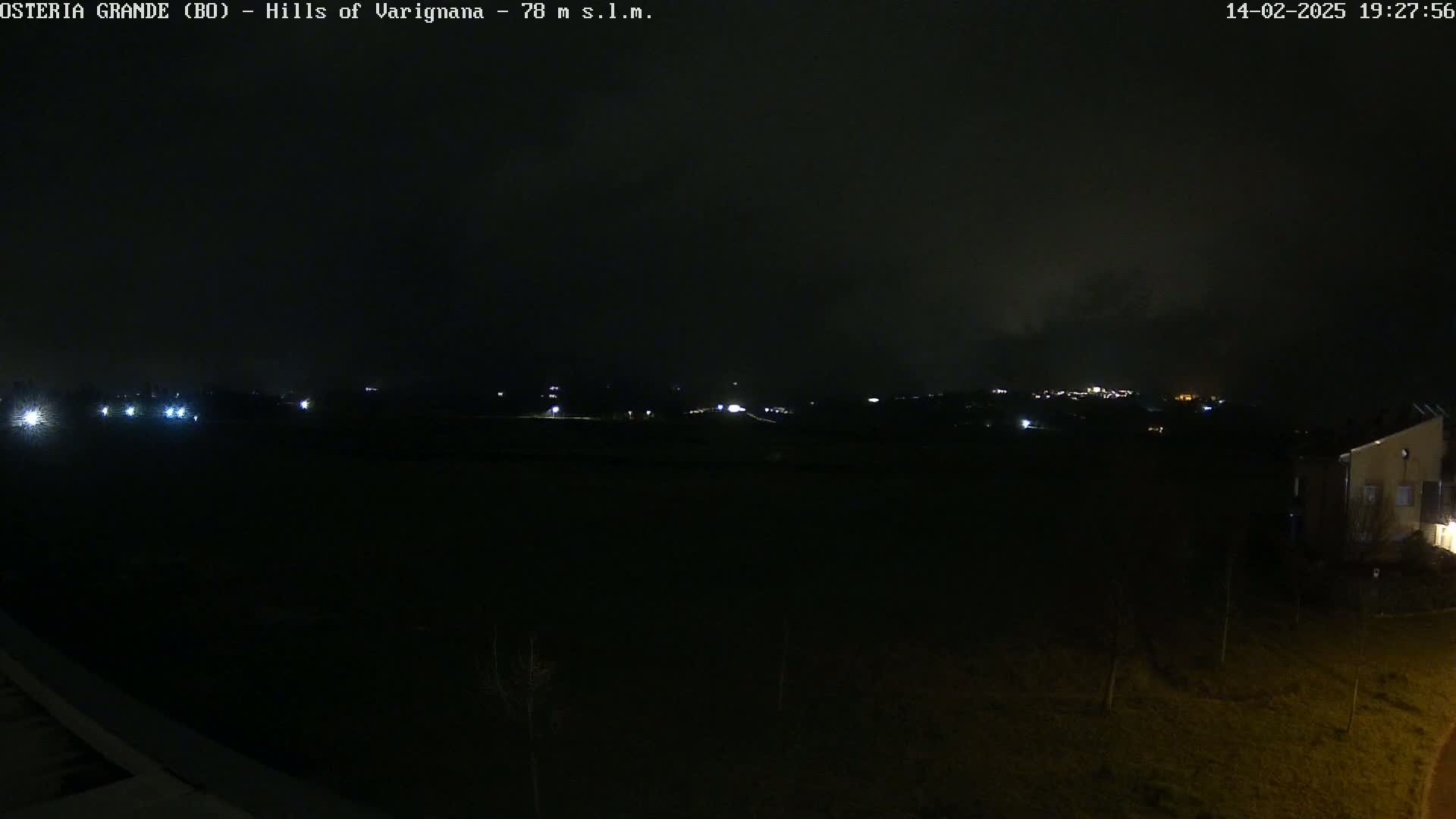 A nighttime view of dimly lit hills and a building, under a dark, cloudy sky.