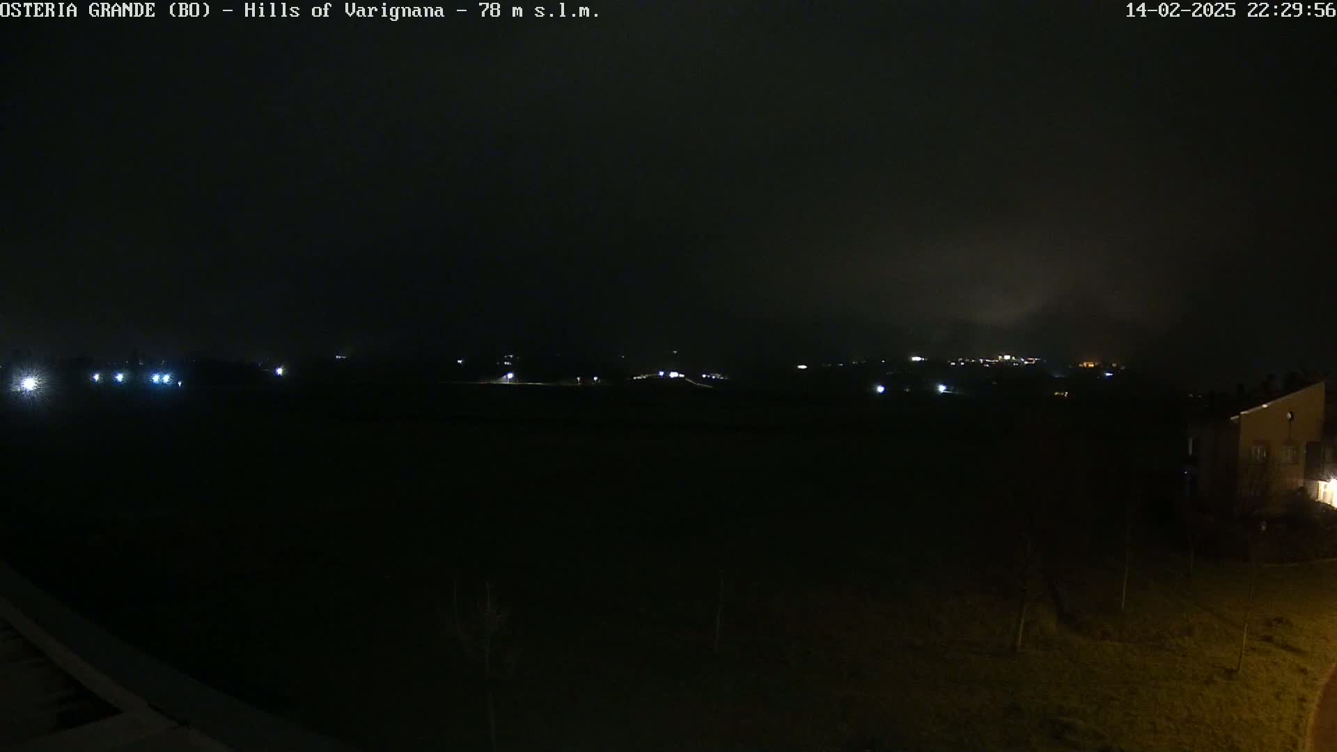 A nighttime, dark, and hazy view of a landscape with a few distant lights, possibly a small town or village, visible in the background.