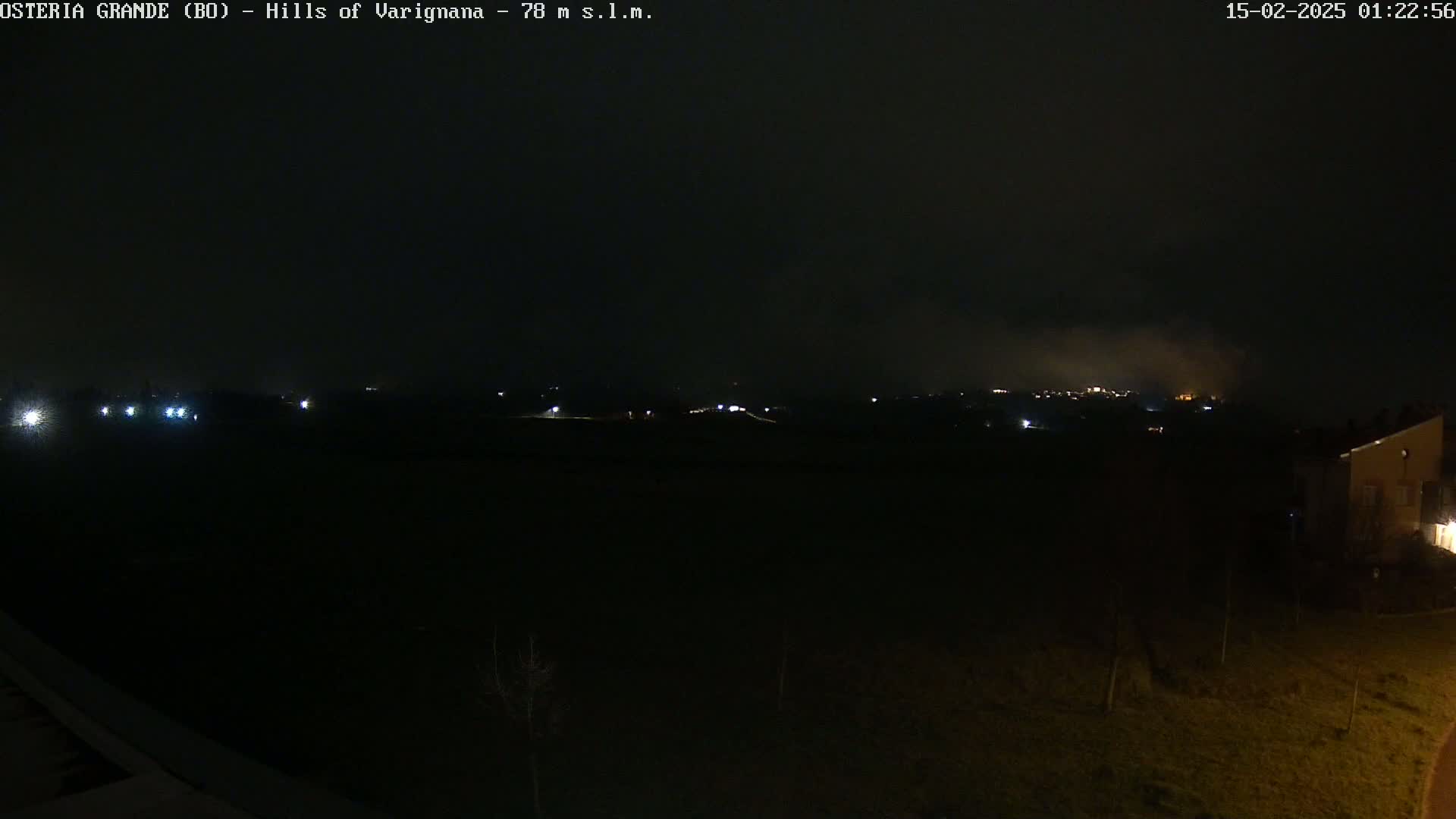 A nighttime, foggy view of dimly lit hills and a few buildings in the distance.