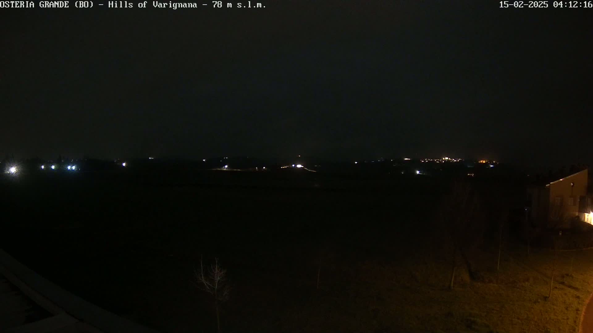 A nighttime view of dimly lit hills and a few buildings under a dark, overcast sky.