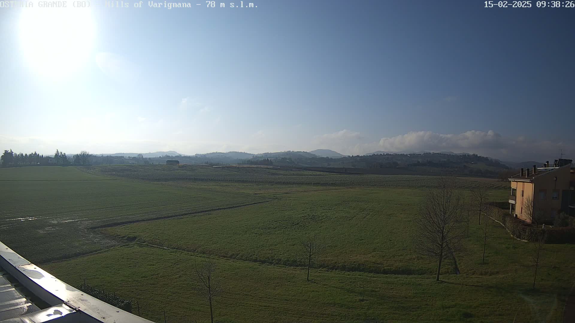 A sunny day reveals a flat expanse of green fields extending to distant hills under a mostly clear blue sky with a few clouds.