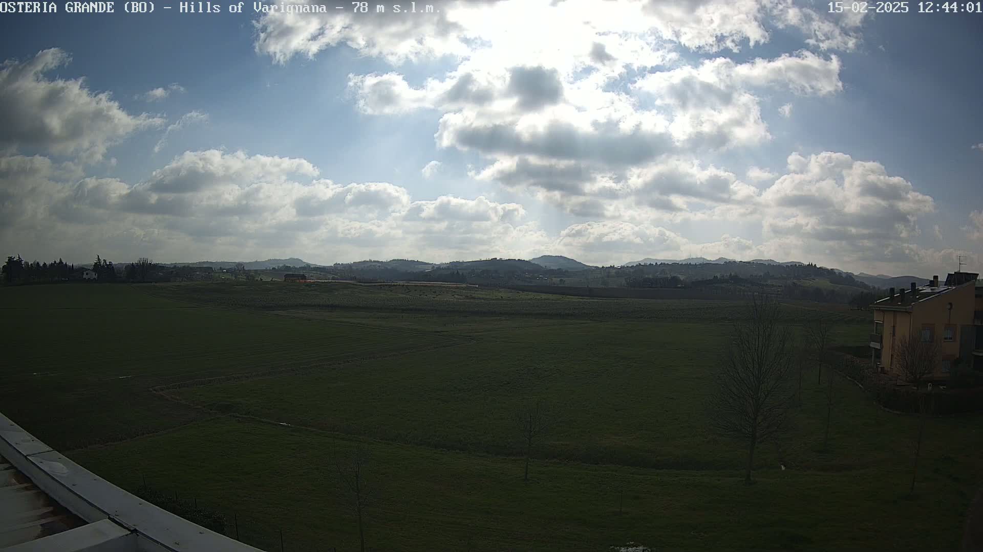 A partly cloudy day reveals a wide expanse of flat, green farmland stretching towards a range of low hills in the distance.