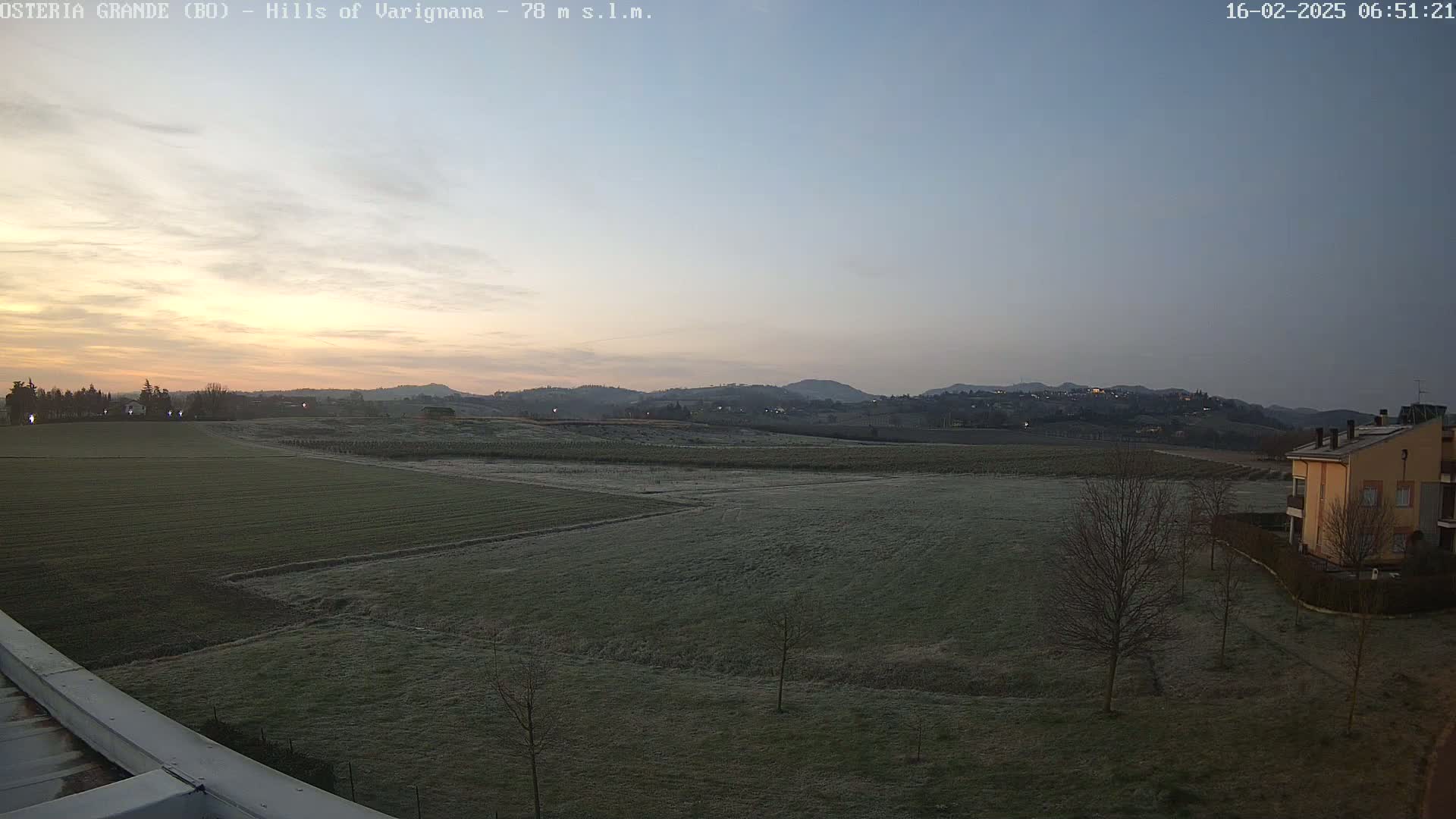 A frost-covered field stretches toward a line of hills at sunrise under a clear, pale sky.