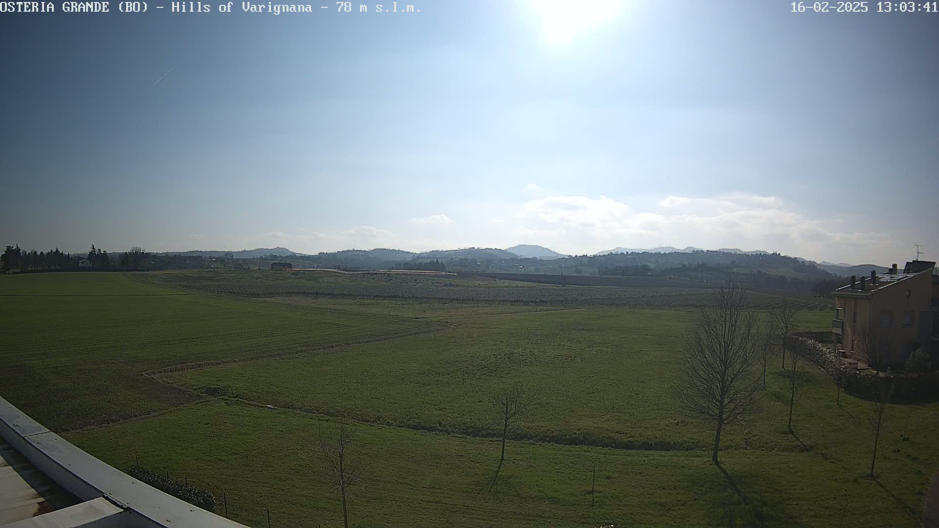 A sunny day reveals a wide expanse of green fields stretching towards a range of distant hills under a mostly clear sky.