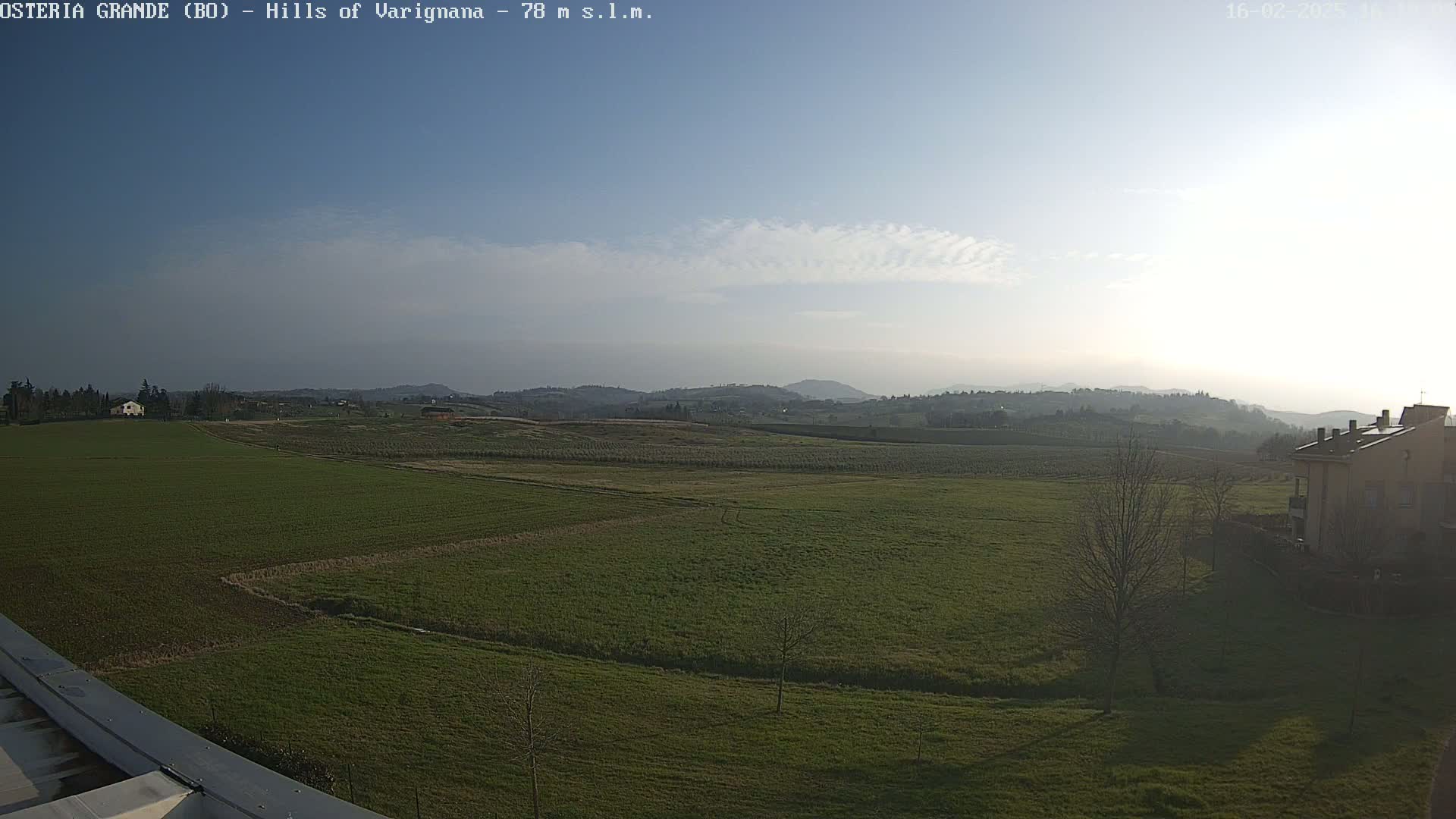 A mostly sunny day reveals a vast expanse of green fields and distant hills under a lightly clouded sky.