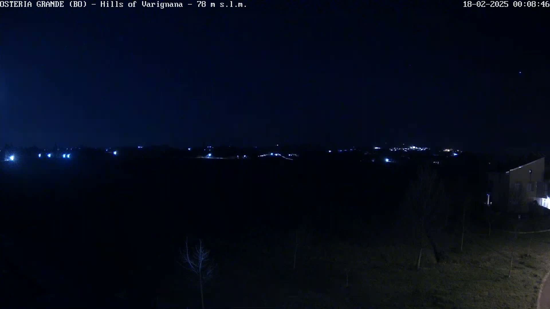 A nighttime view of a dark landscape with a few scattered lights in the distance, under a clear, dark sky.