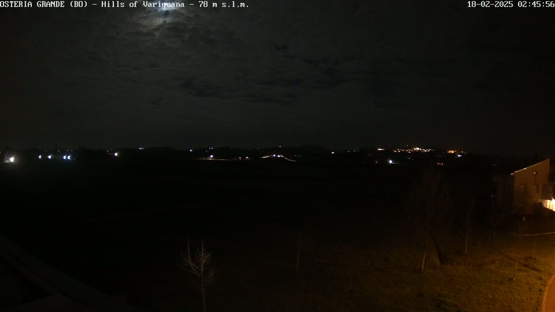 A nighttime view of dimly lit hills and a few buildings under a mostly cloudy sky.