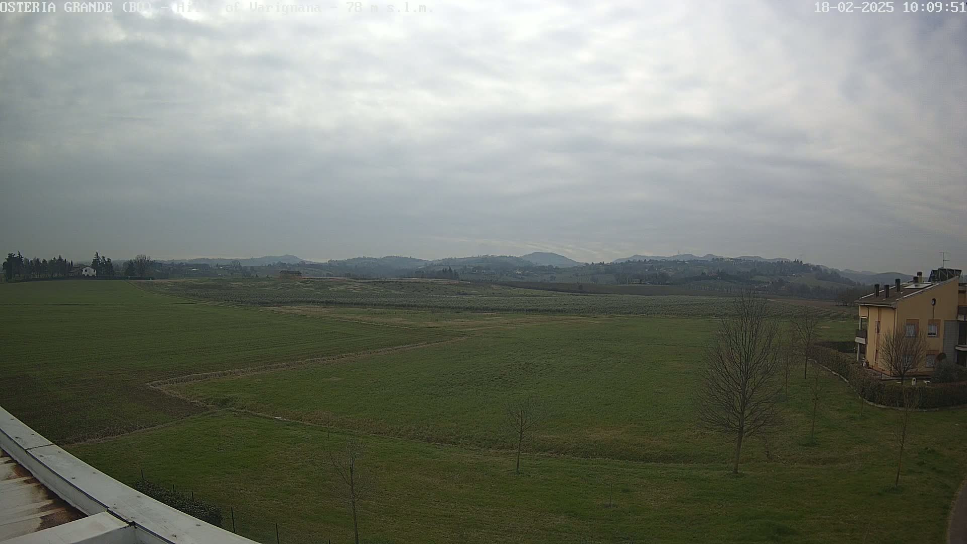 A wide, flat expanse of green farmland stretches to distant hills under a cloudy sky.