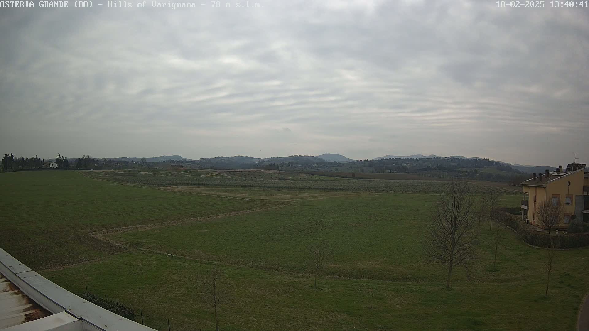 A wide, flat expanse of green farmland stretches to distant, rolling hills under a cloudy sky.