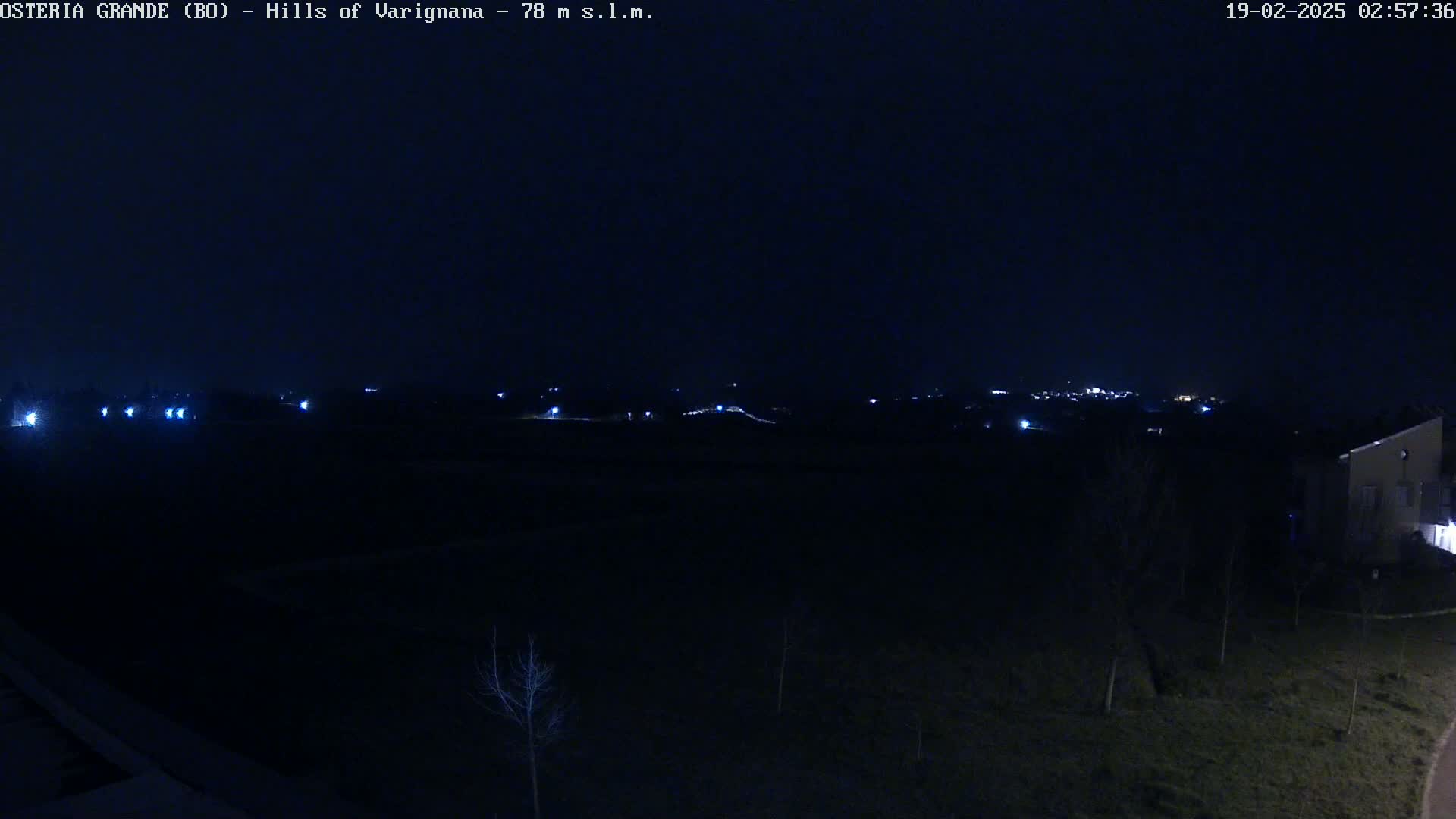 A dark, nighttime landscape shows a distant, faintly lit town under a clear, black sky.