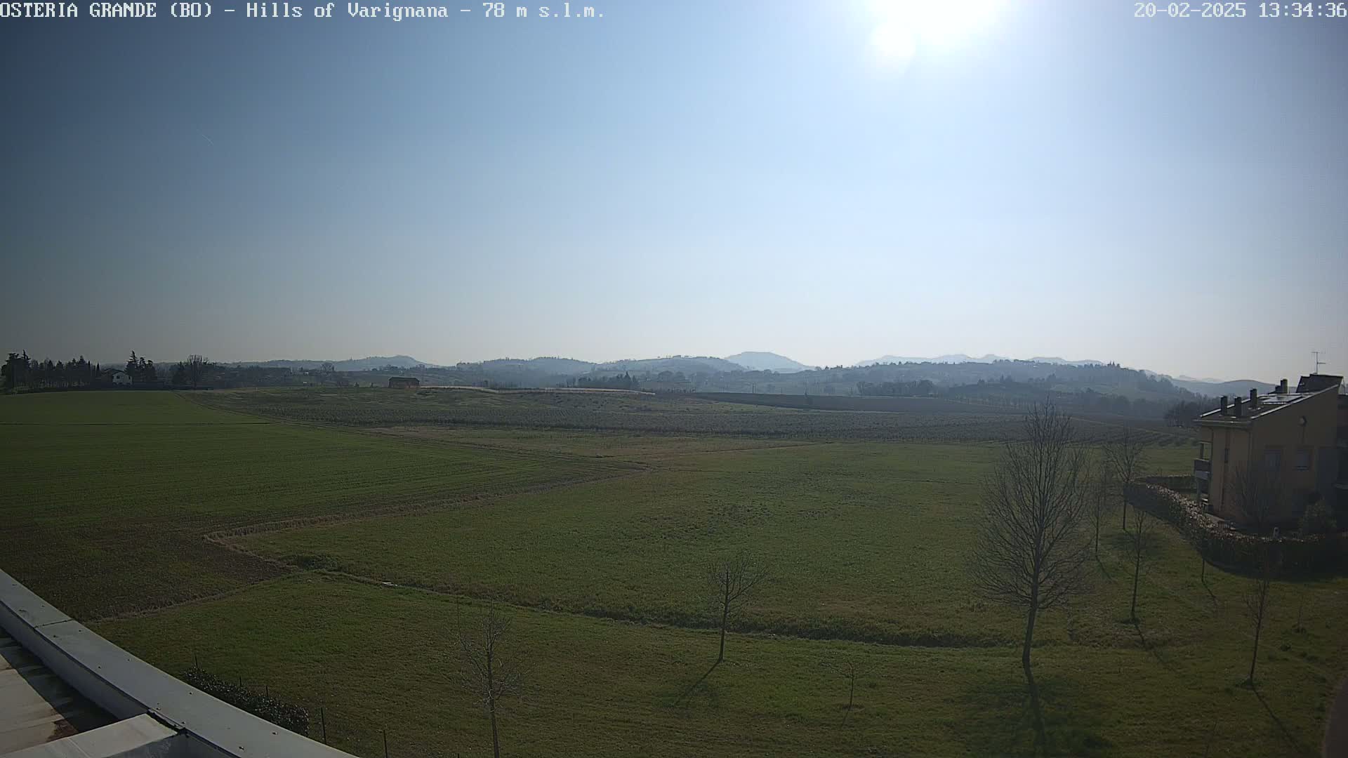 A sunny day reveals a vast, flat expanse of green fields stretching towards distant, hazy hills under a clear blue sky.