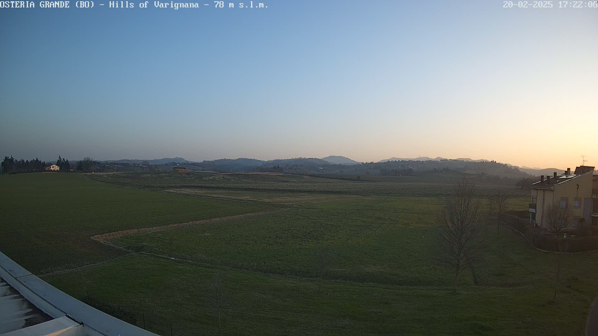 A flat, green field stretches out to rolling hills under a clear, twilight sky.