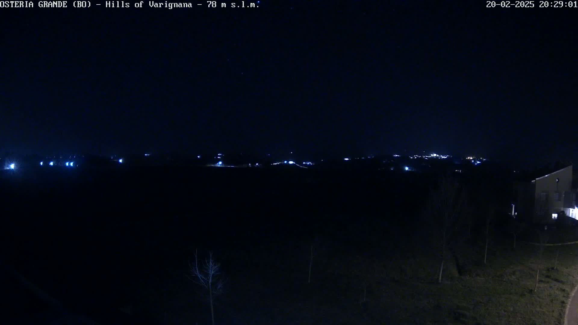 A nighttime, dark view of a sparsely lit landscape with a distant town or city visible on the horizon under a clear, starless sky.