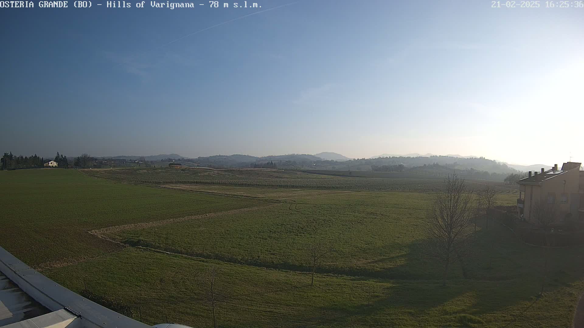 A wide, flat expanse of green fields stretches to rolling hills under a clear, light-blue sky.