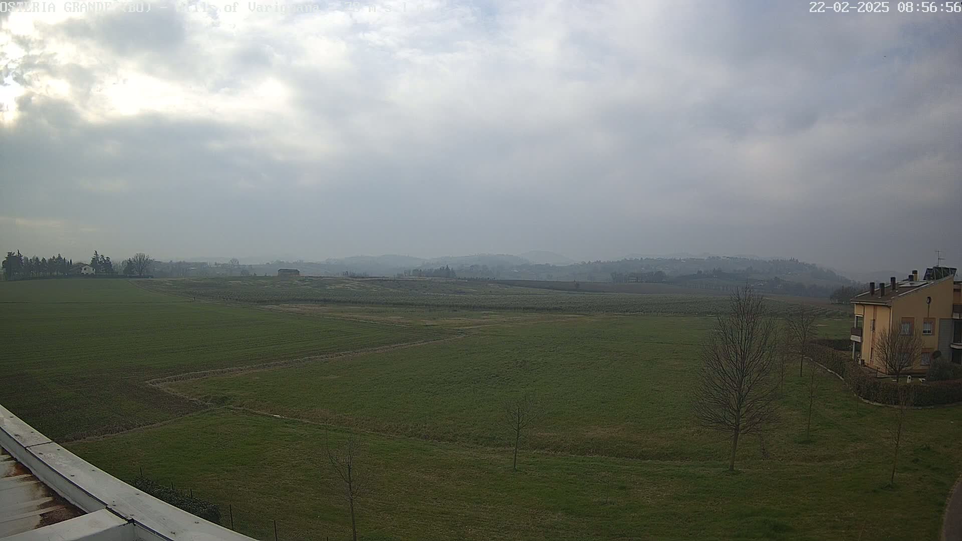 A flat, green field stretches to distant, hazy hills under a mostly cloudy sky.