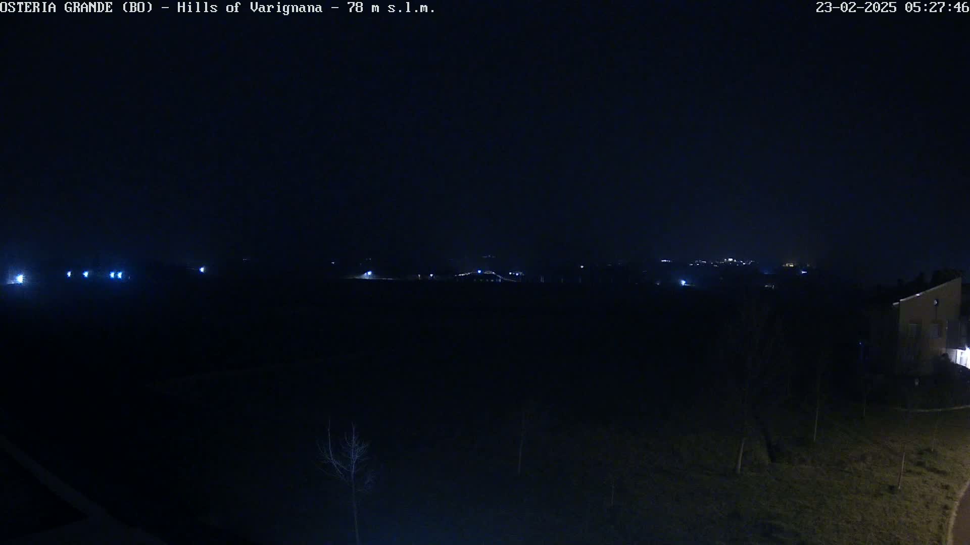A nighttime, dark view of sparsely lit hills and a building in the lower right corner.