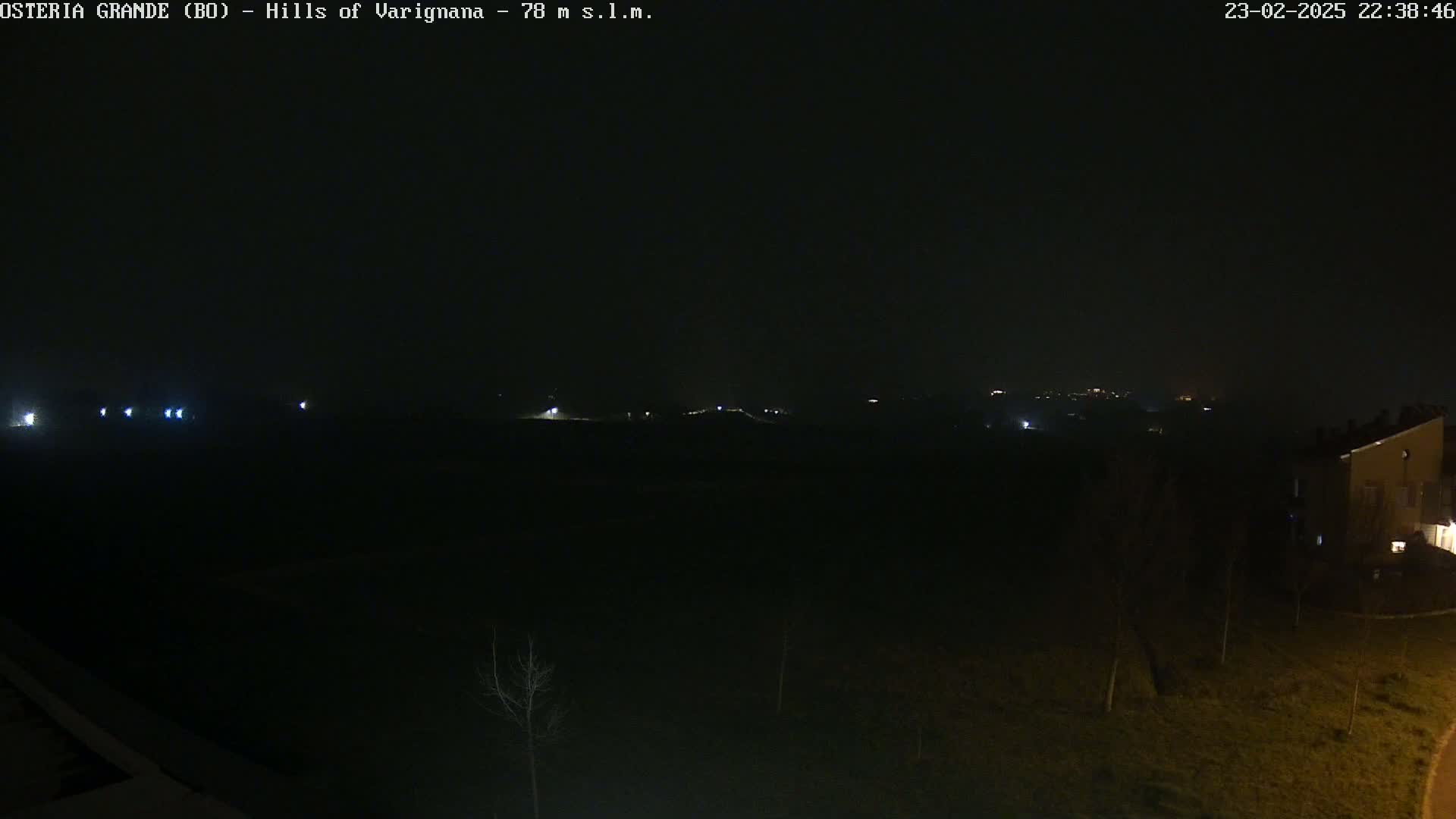 A nighttime view of dark, sparsely vegetated land with a few distant lights and a building visible on the right.