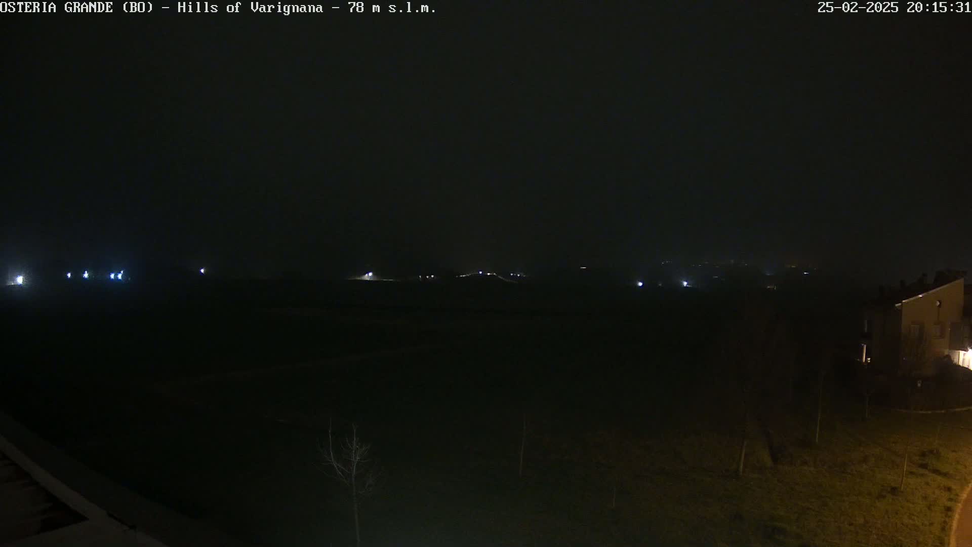A dark, nighttime landscape is visible, with a few faint lights in the distance and a building partially visible in the lower right corner.