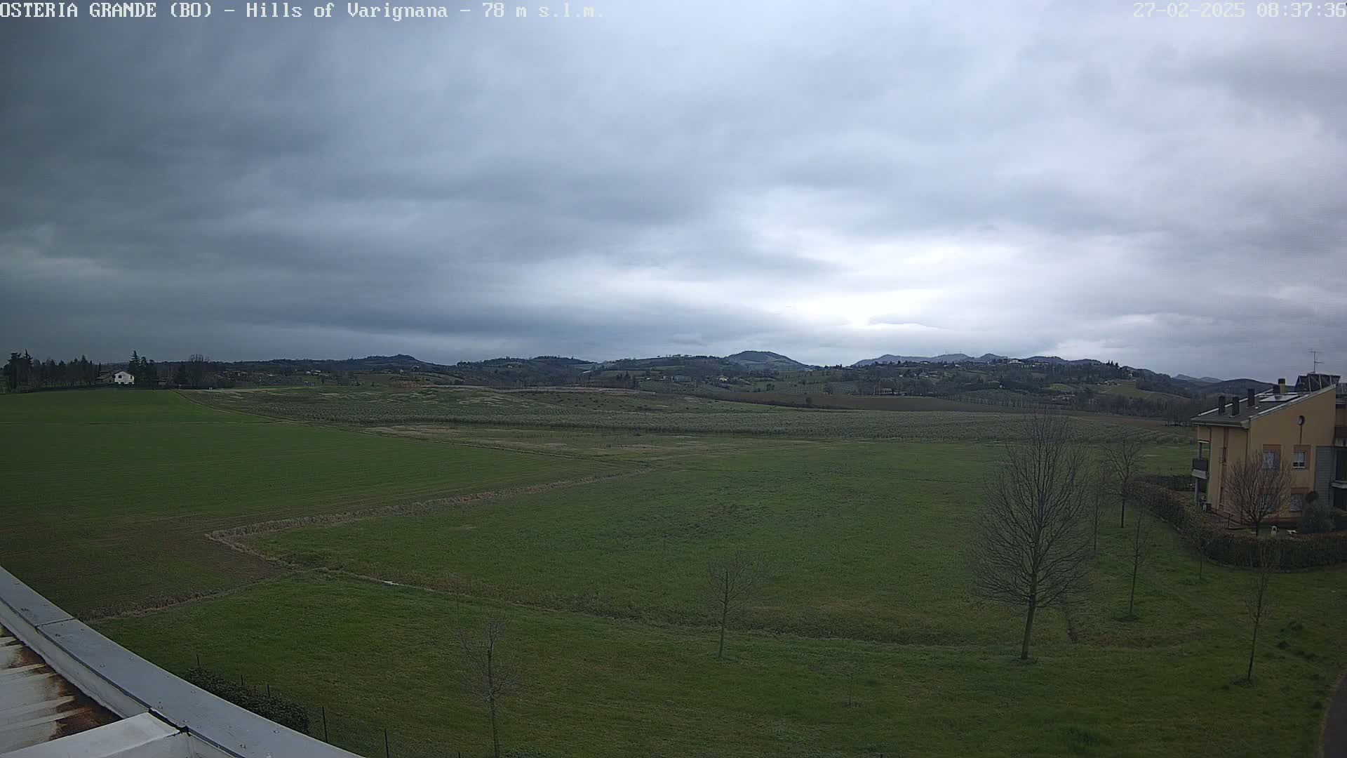 A wide, flat expanse of green farmland stretches to rolling hills under a cloudy sky.