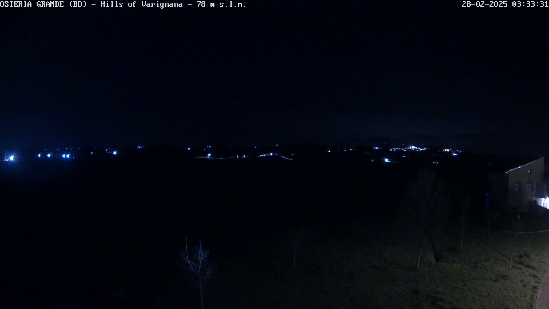 A dark, nighttime landscape shows a distant, faintly lit town in the background under a clear, starlit sky.