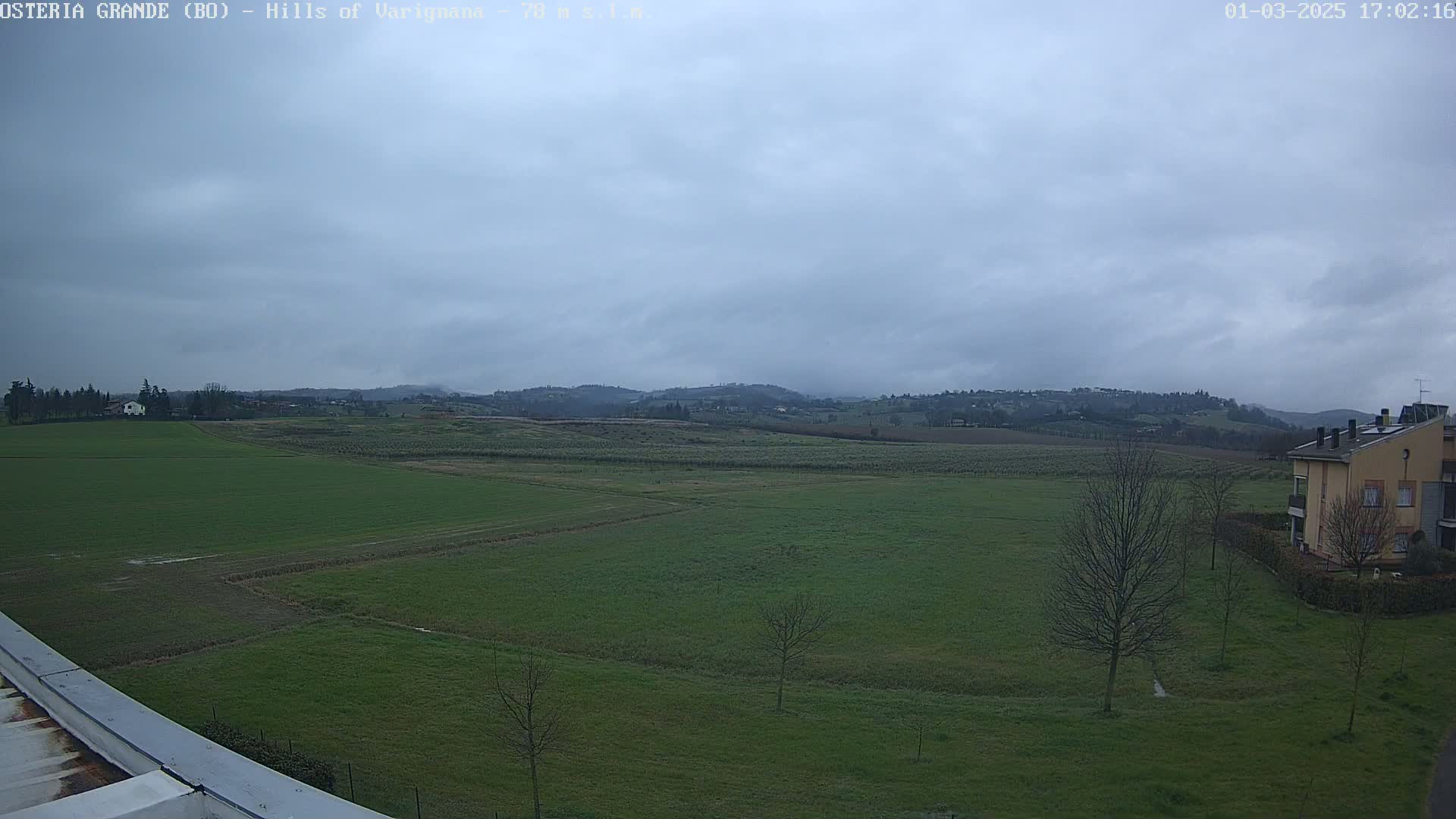 A wide, green field stretches to rolling hills under a cloudy sky.