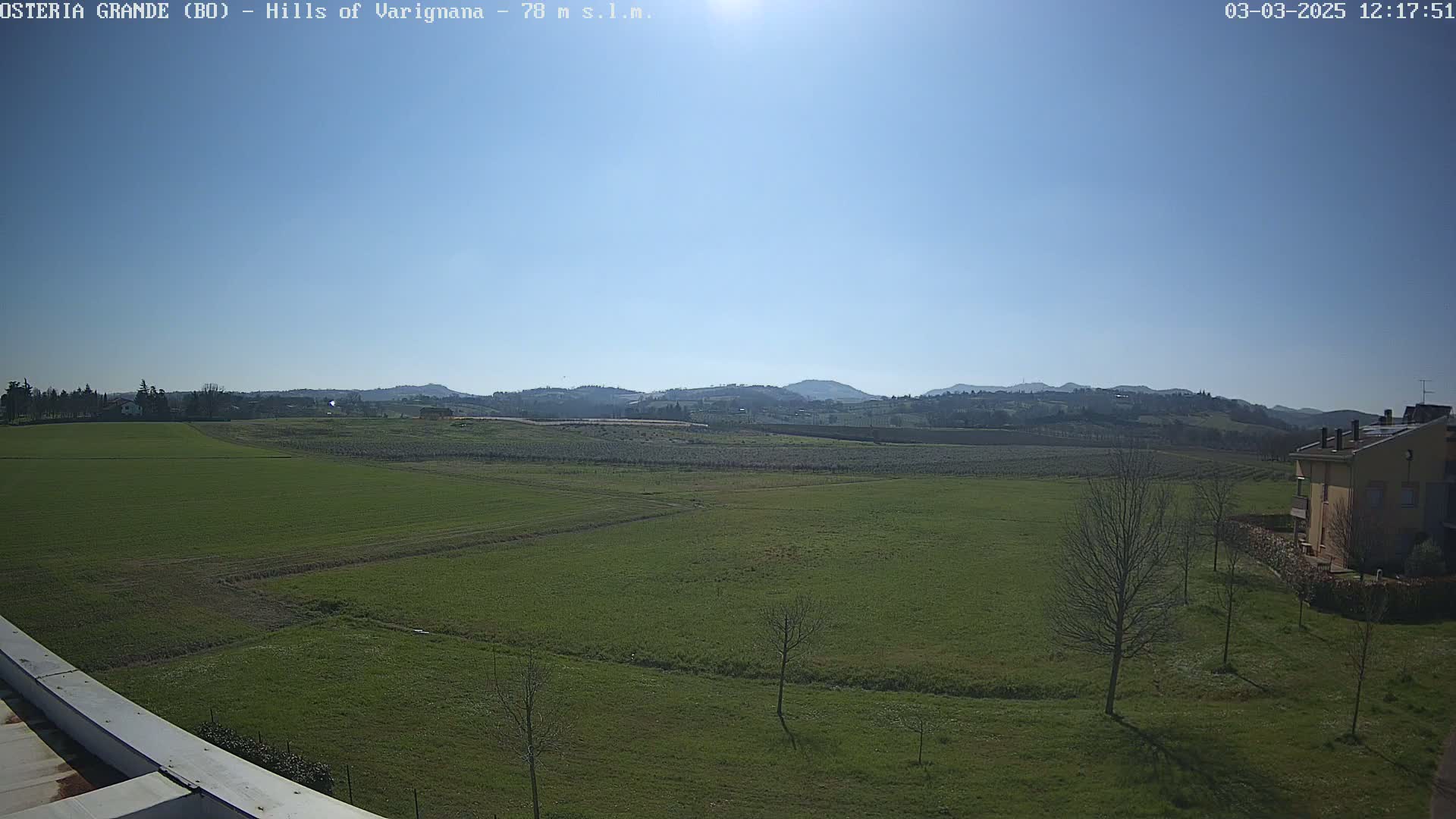 A sunny day reveals a wide expanse of green fields stretching towards distant hills under a clear blue sky.