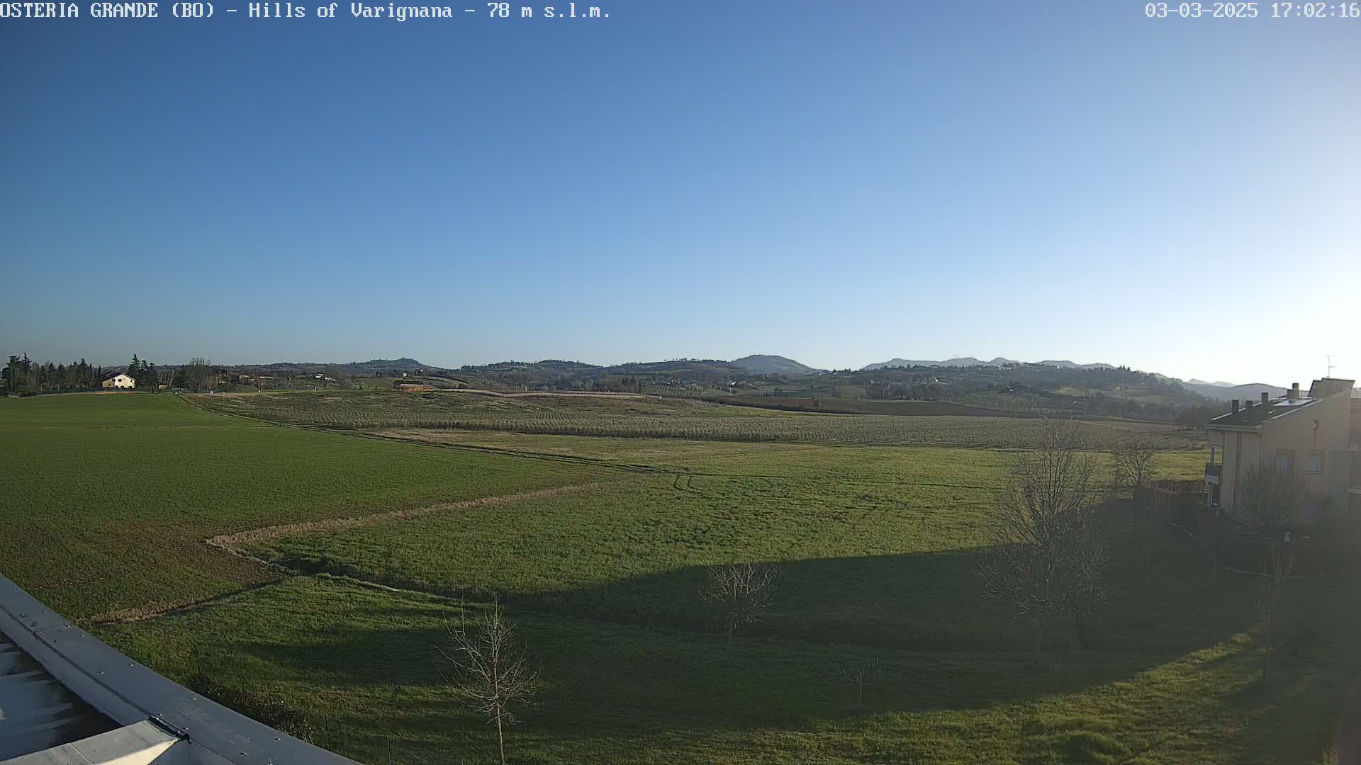 A wide, flat field of green grass stretches out to rolling hills under a clear blue sky.
